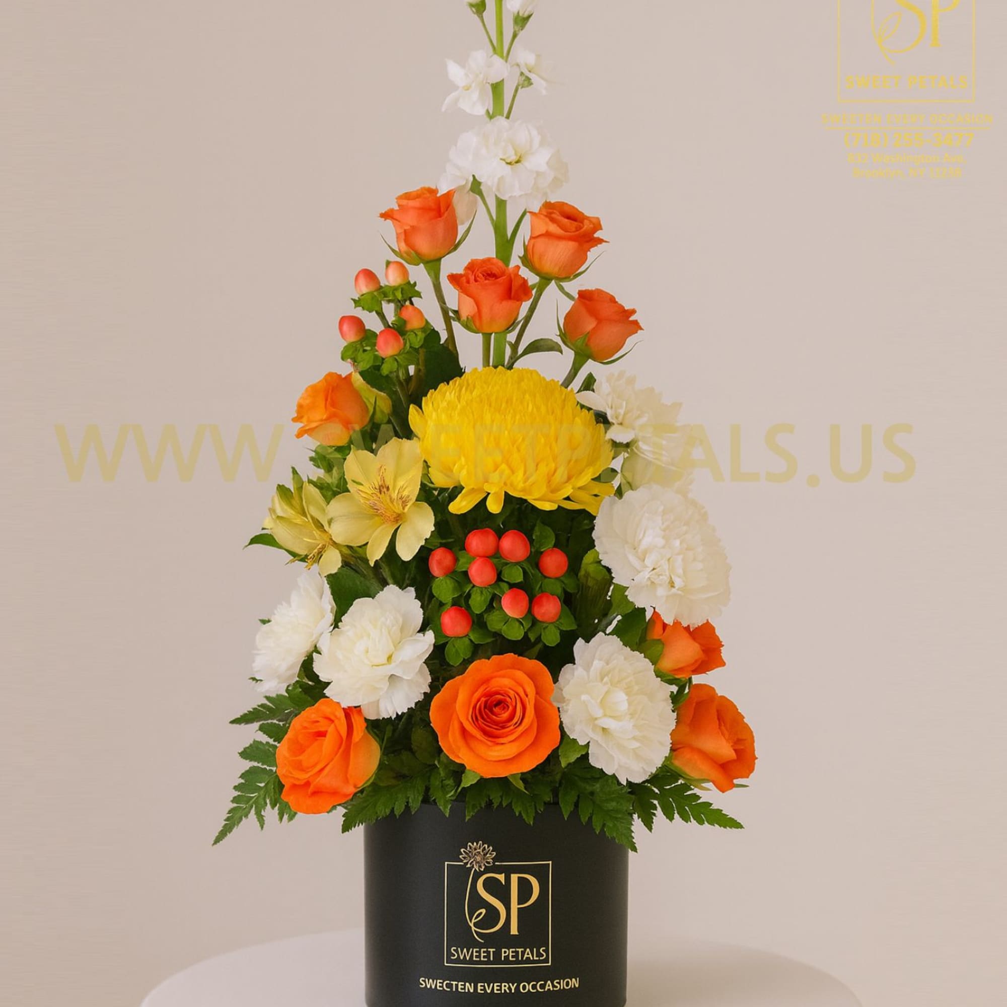 Orange roses and white flowers in a black hatbox with yellow blooms