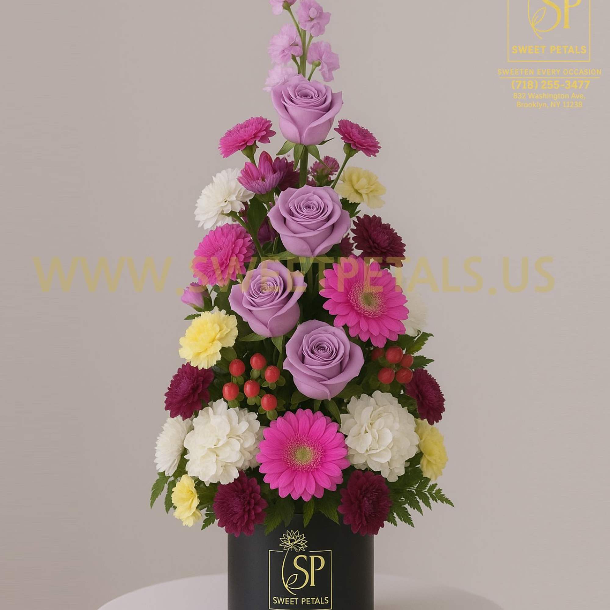 Tall arrangement of lavender roses, pink daisies, and mixed blooms in a black box