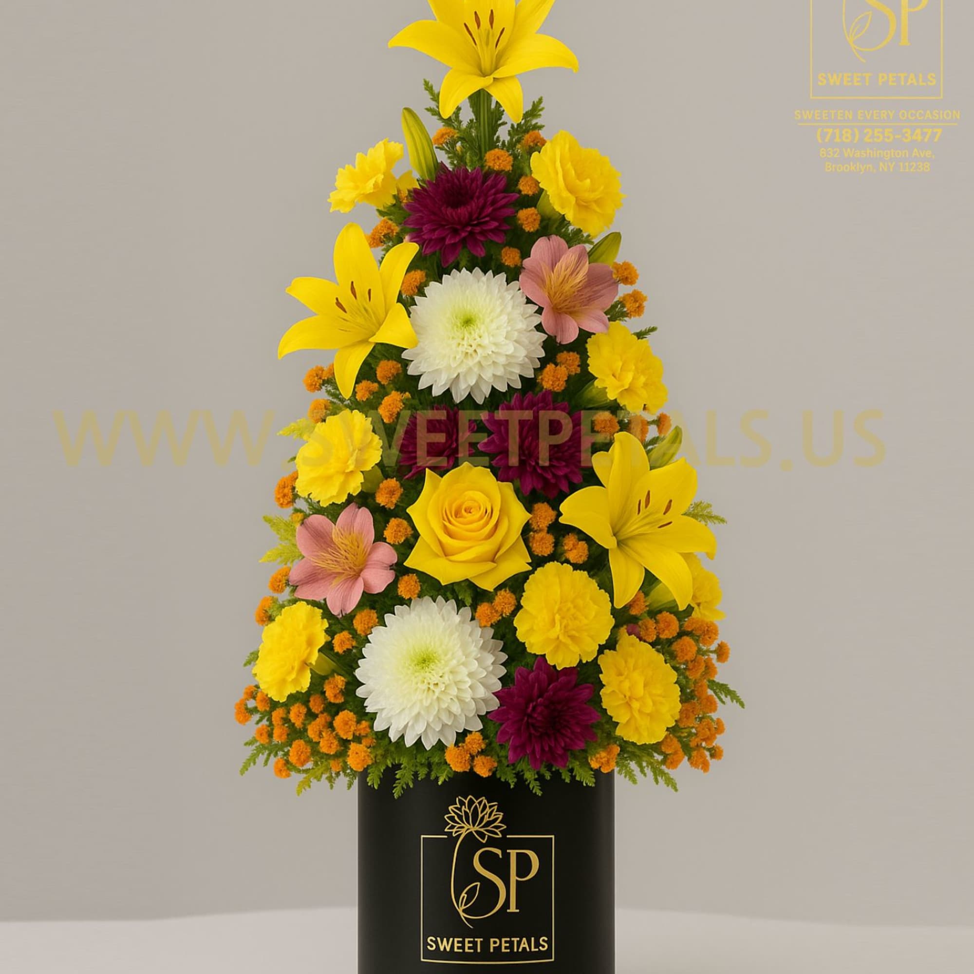 Tiered floral arrangement in a black cylinder vase with yellow lilies and mixed blooms