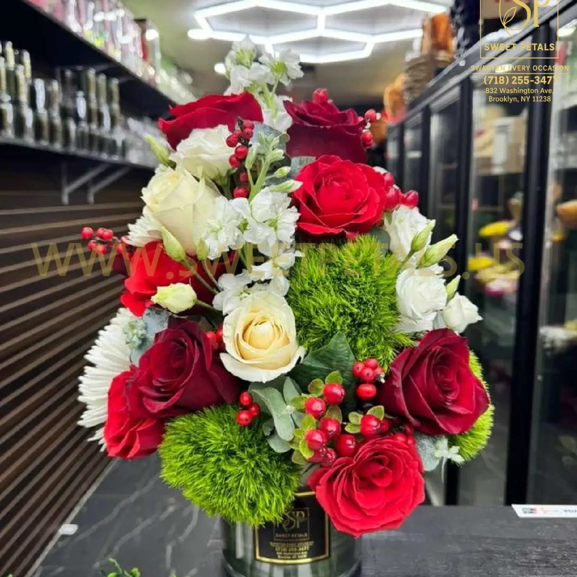 Red and white roses arranged in a metal vase with bright green pom-pom accents.