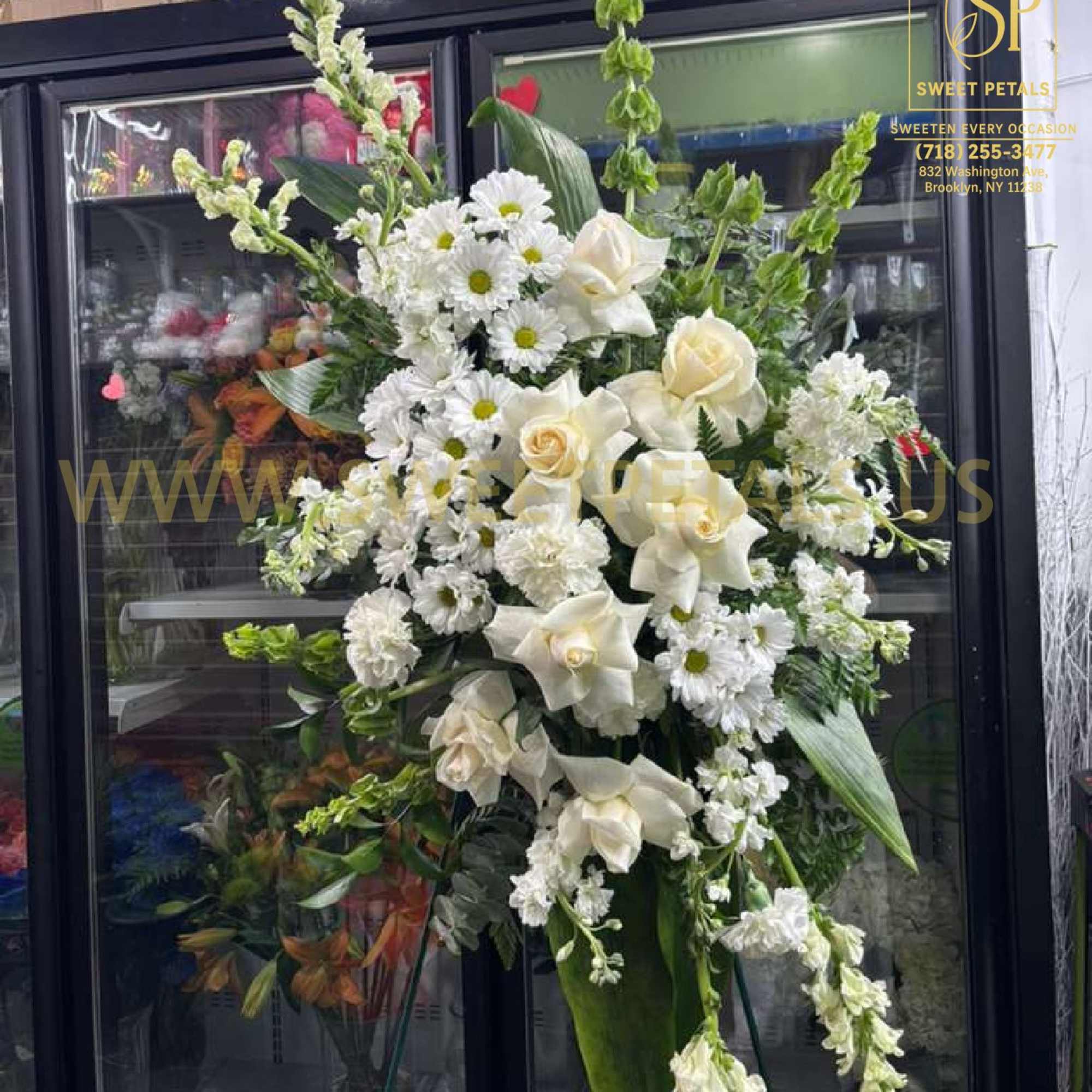 Tall white floral standing arrangement with roses, daisies, and calla lilies