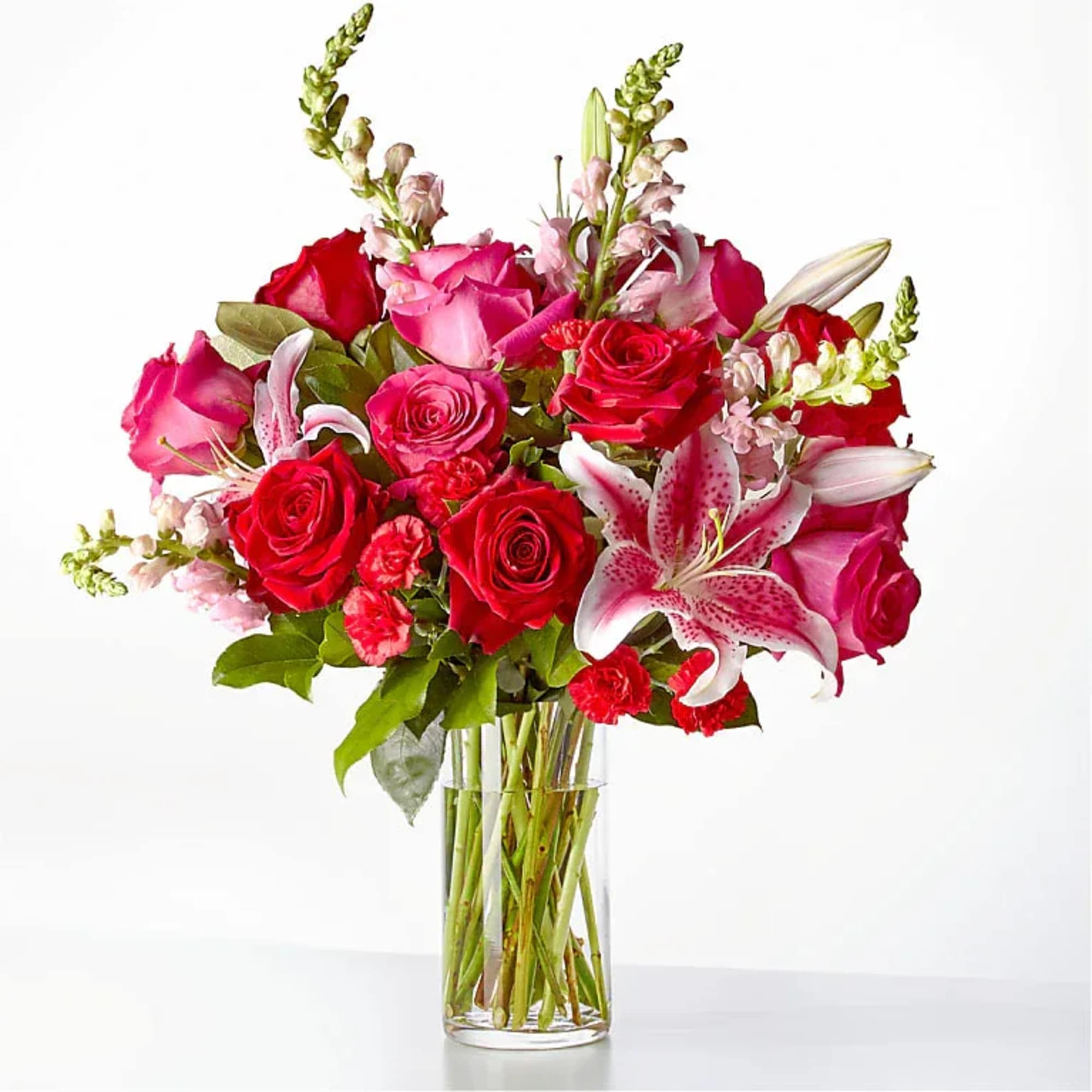 Red and pink roses with lilies in a clear glass vase