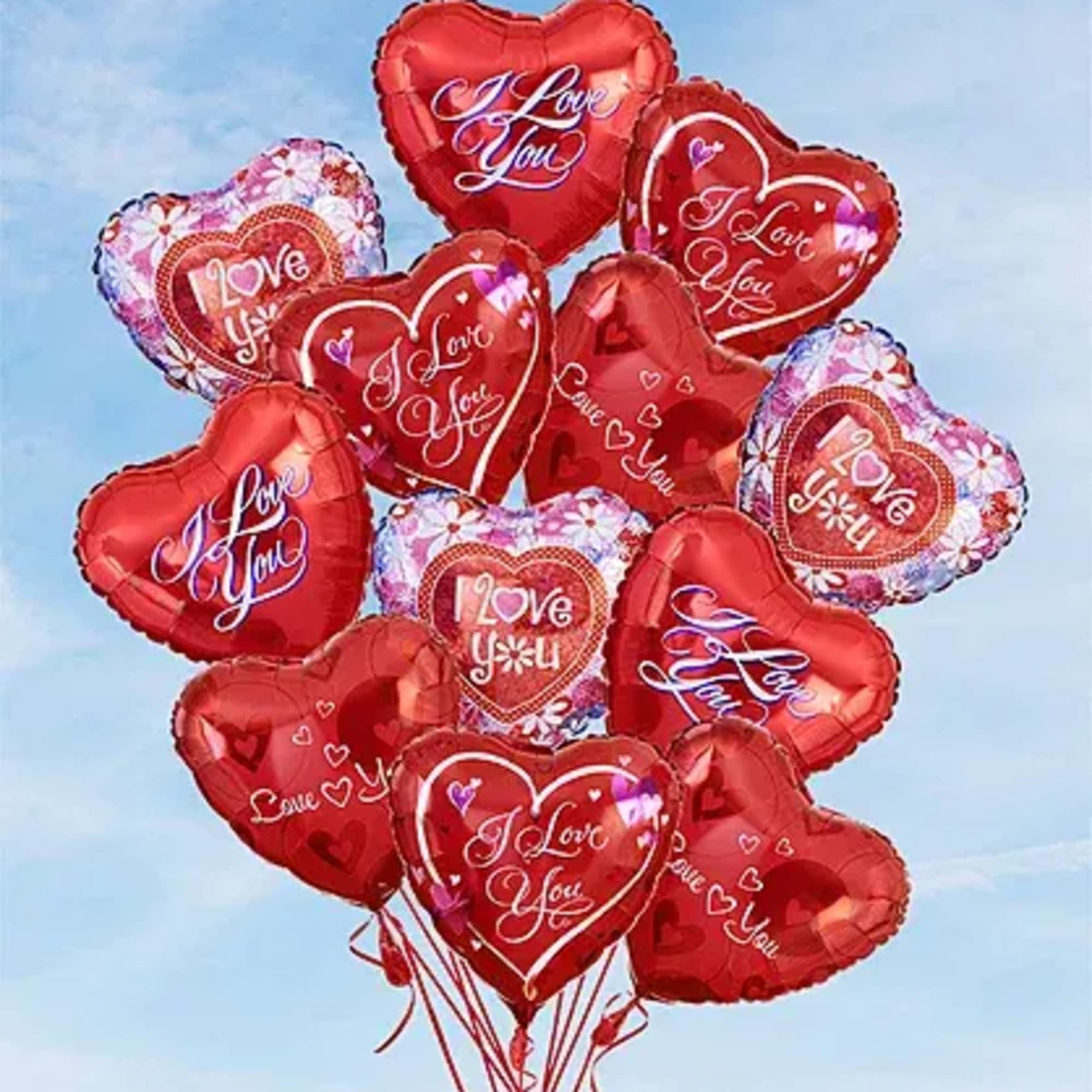 Cluster of red heart-shaped balloons with "Love You" text against a blue sky.