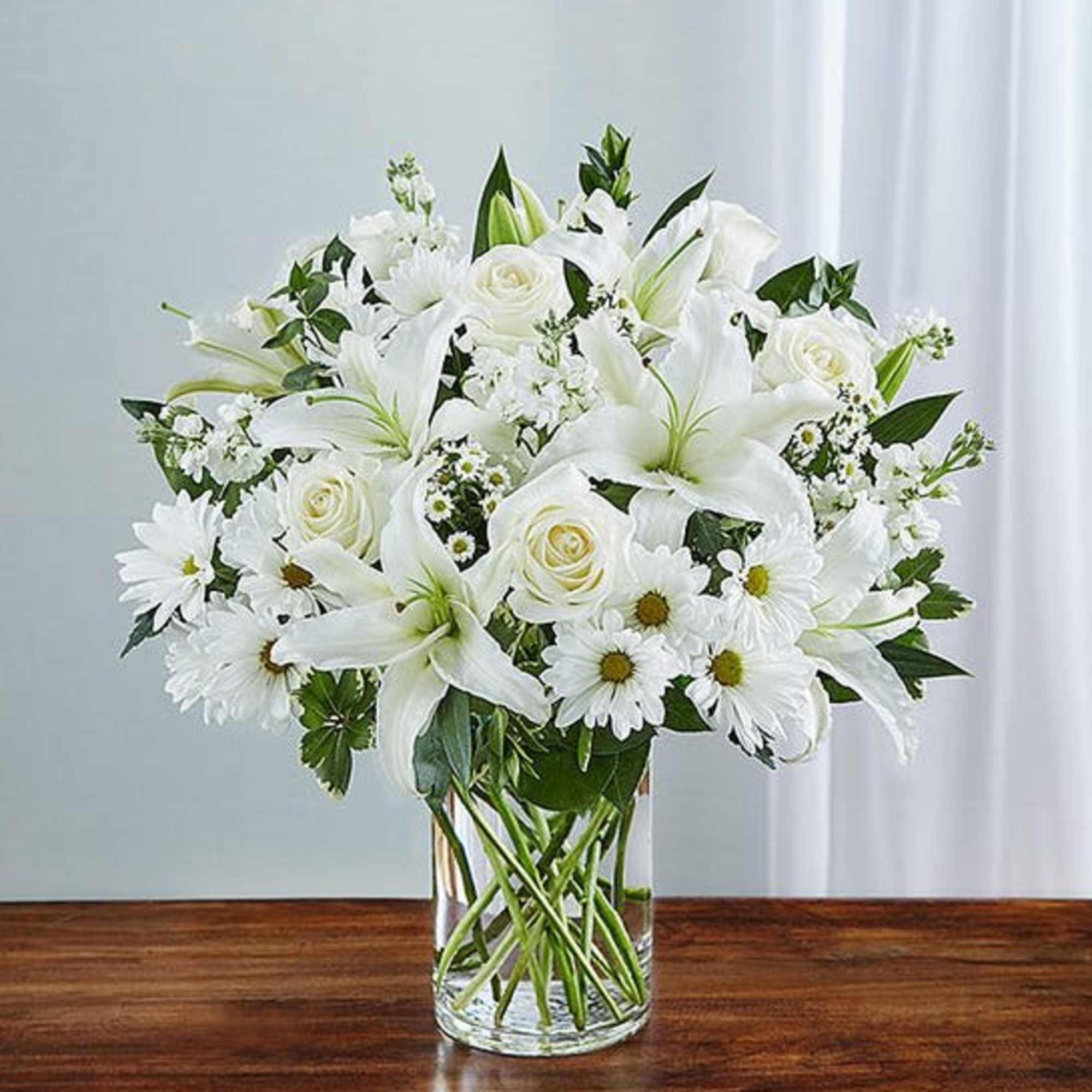 Express your sincere condolences with our elegant all-white arrangement of roses, lilies