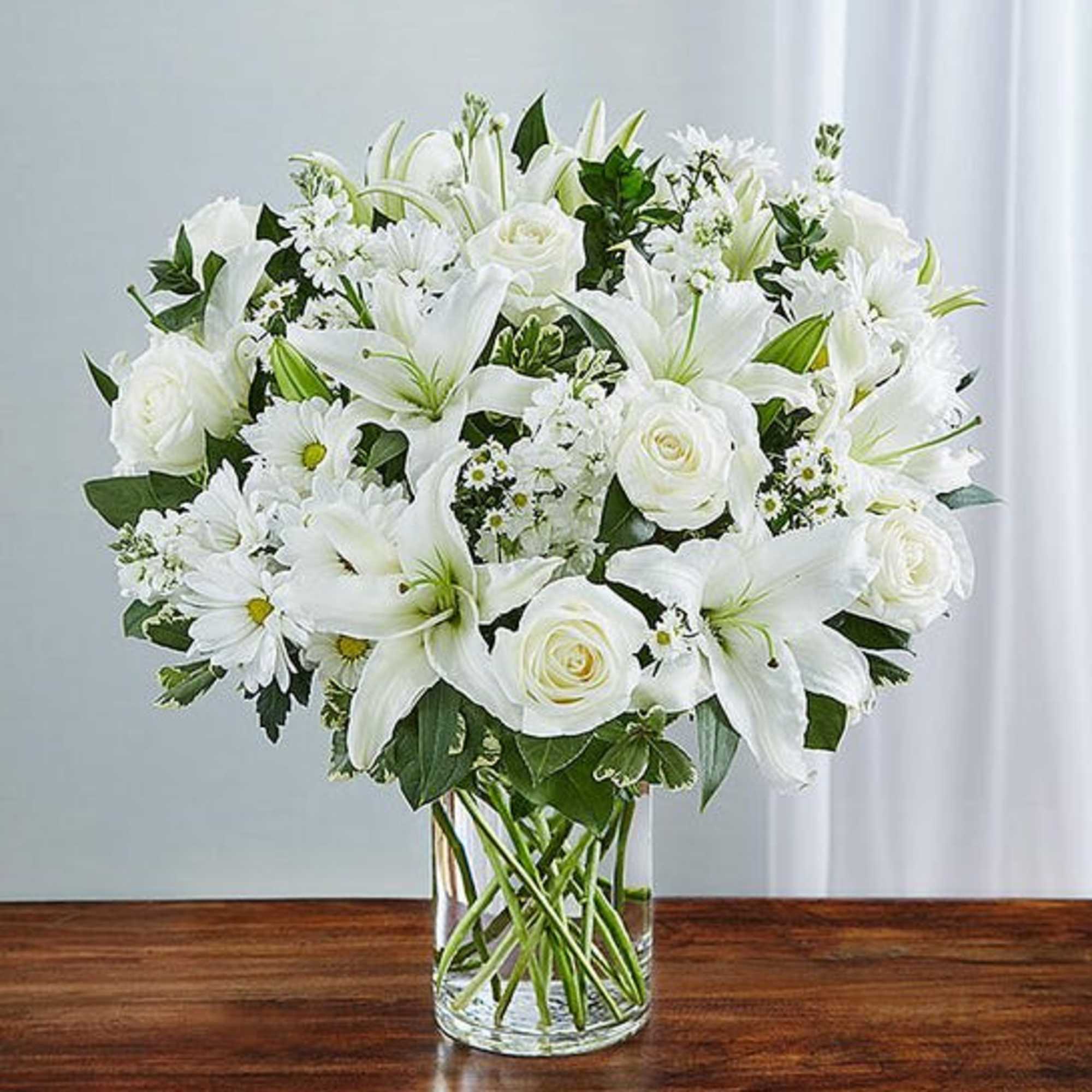 Express your sincere condolences with our elegant all-white arrangement of roses, lilies