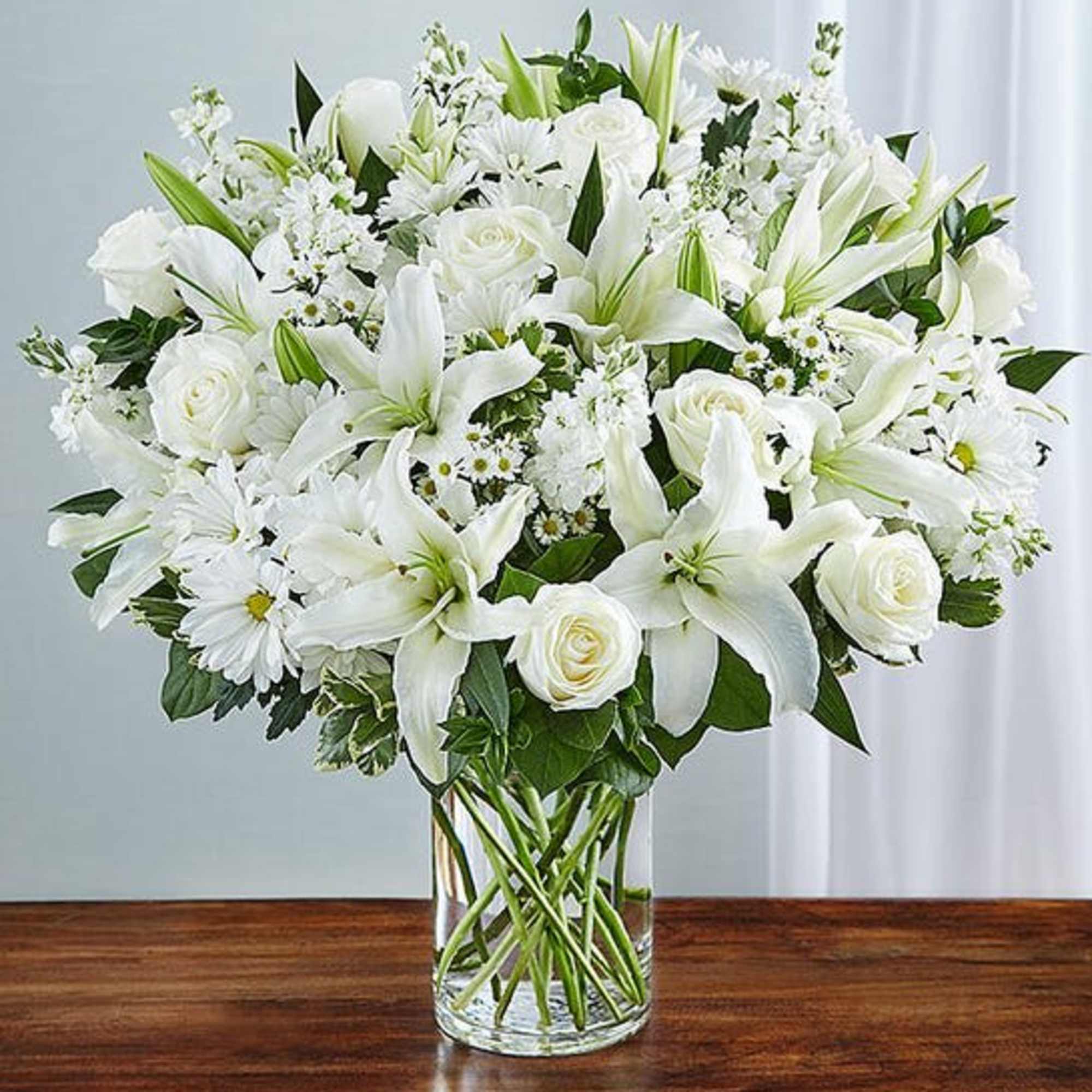 Express your sincere condolences with our elegant all-white arrangement of roses, lilies