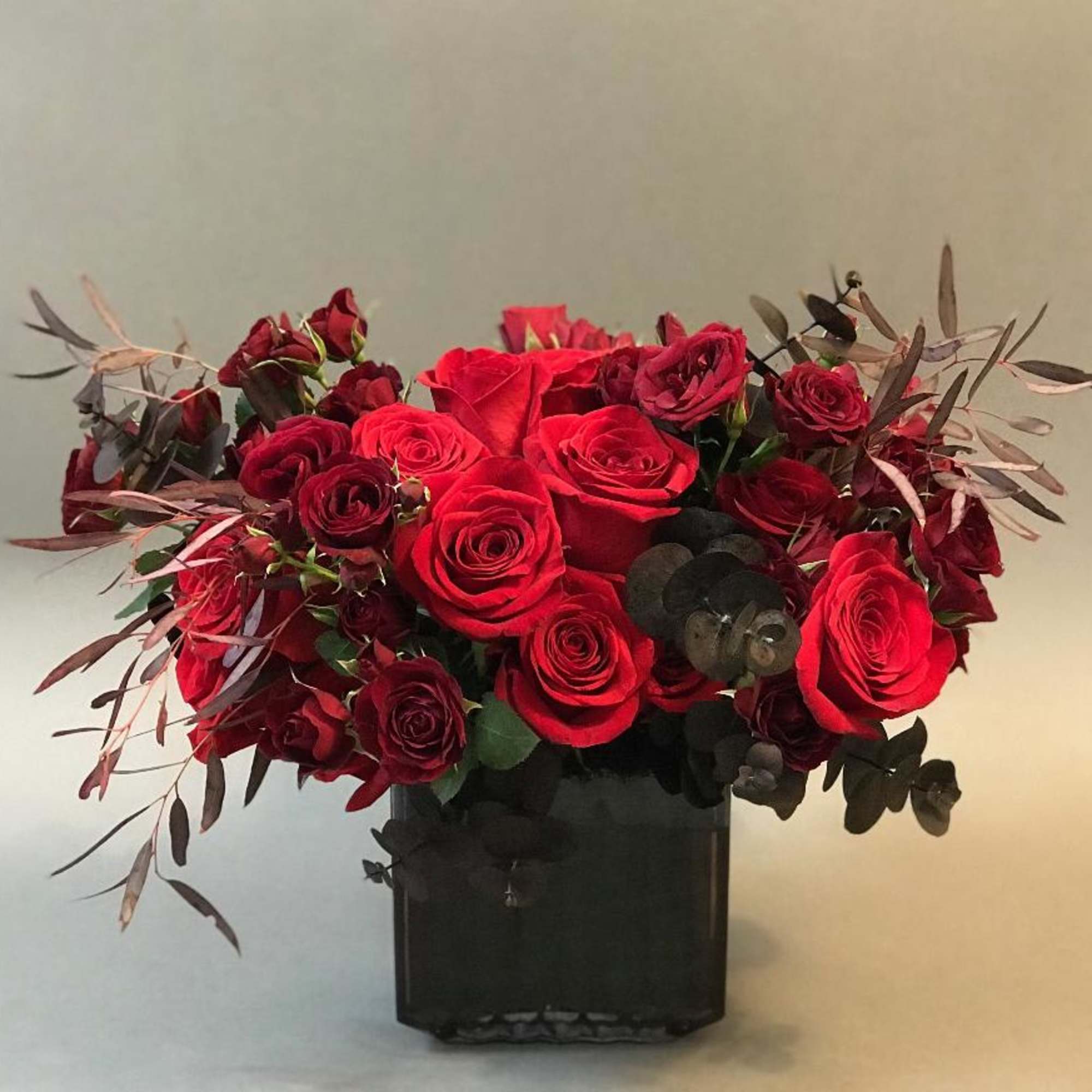 Smoke glass vase with abundant blooms of reds and burgundy roses