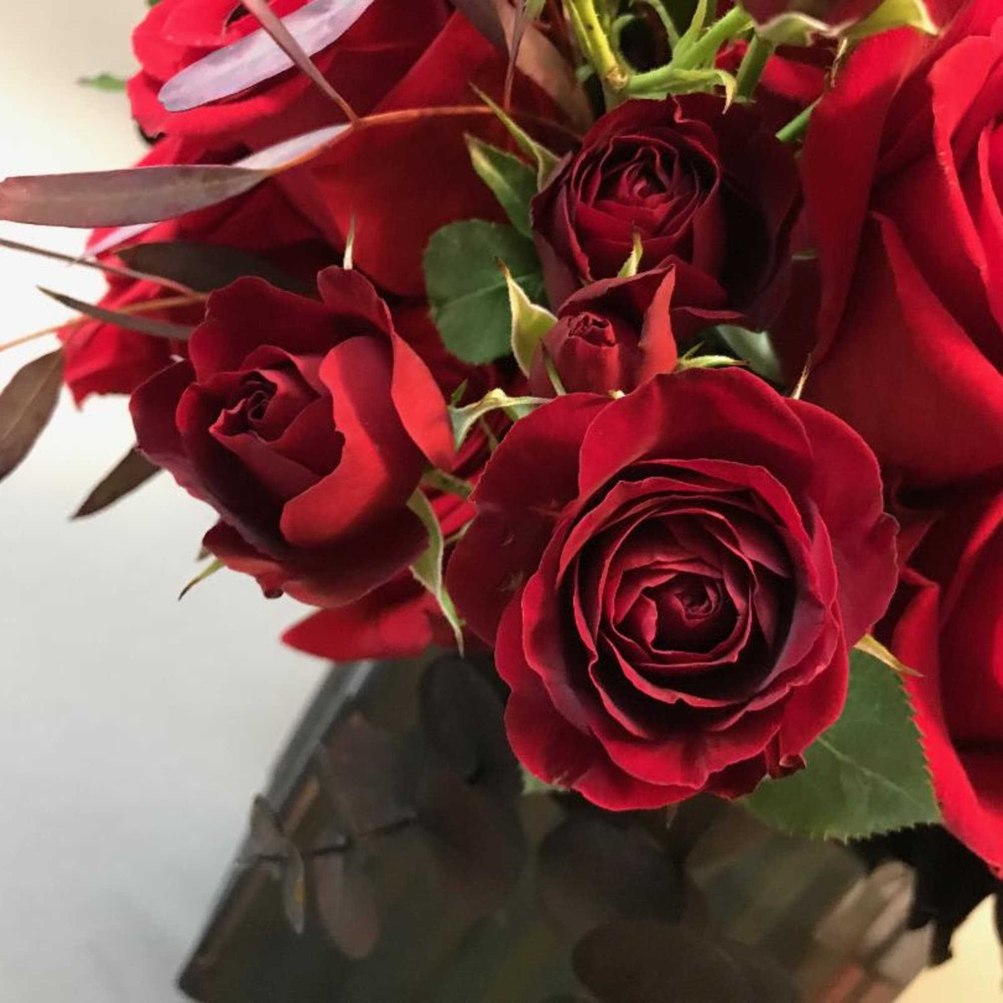Smoke glass vase with abundant blooms of reds and burgundy roses
