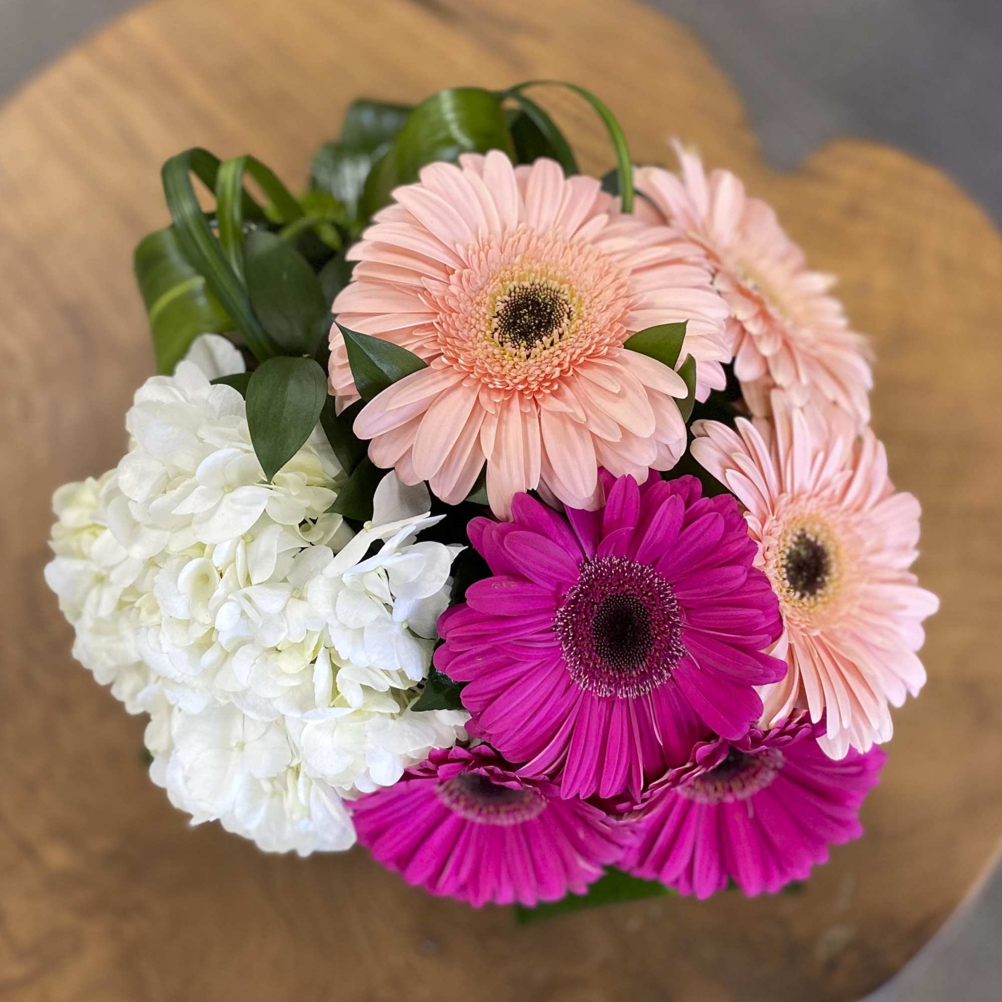 This luscious arrangement of Gerber daisies, hydrangeas and other seasonal flowers and