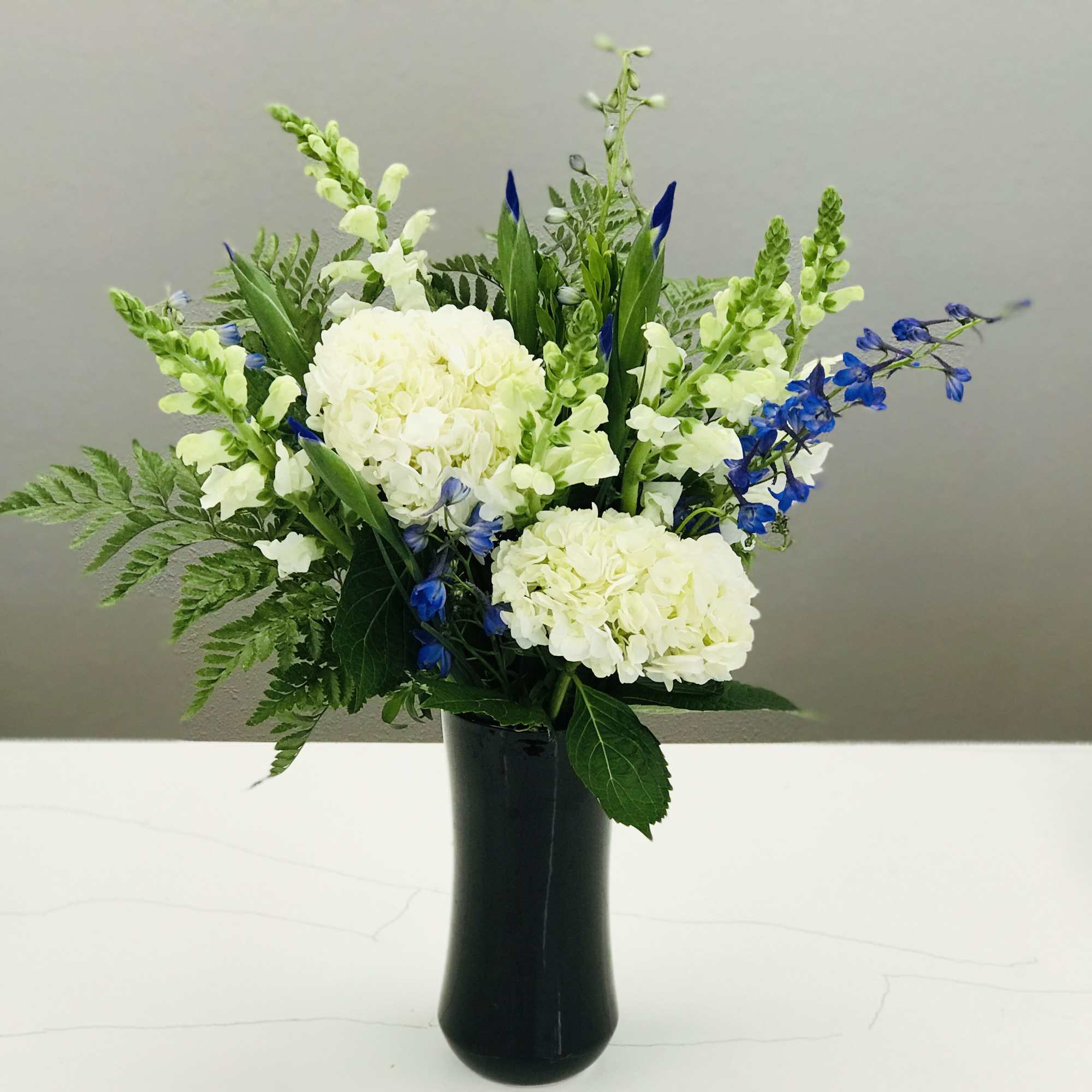 Elegant white flowers with pops of blue in a tall black vase