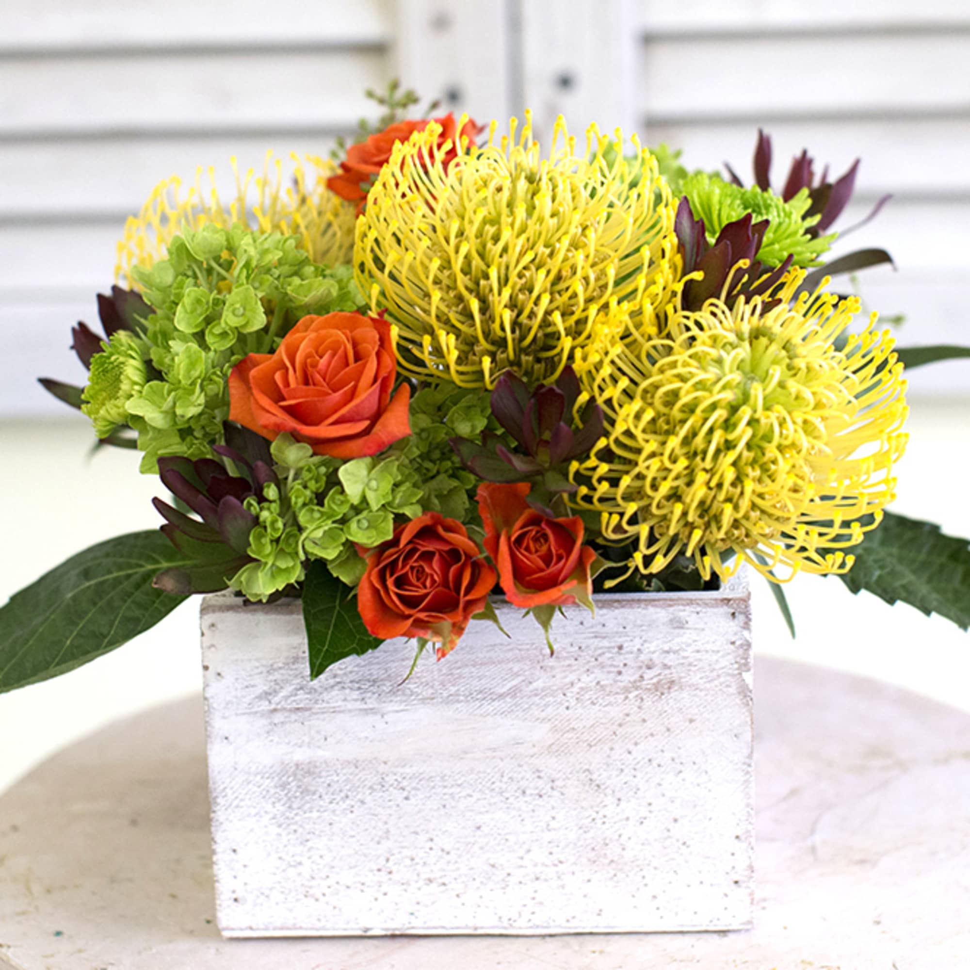 Three yellow protea, green hydrangea, orange spray roses, green yoko ono poms