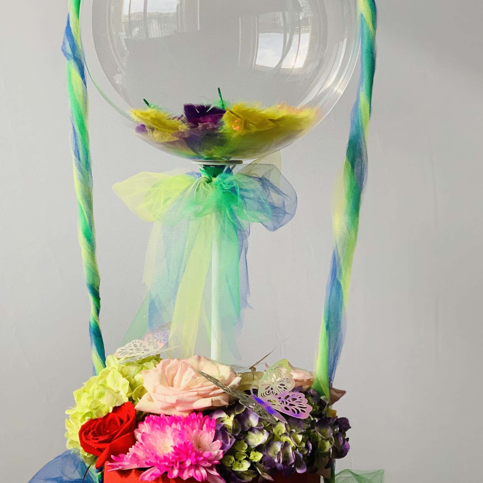Fresh bright color  flower arrangement with fathers inside the bubble balloon.