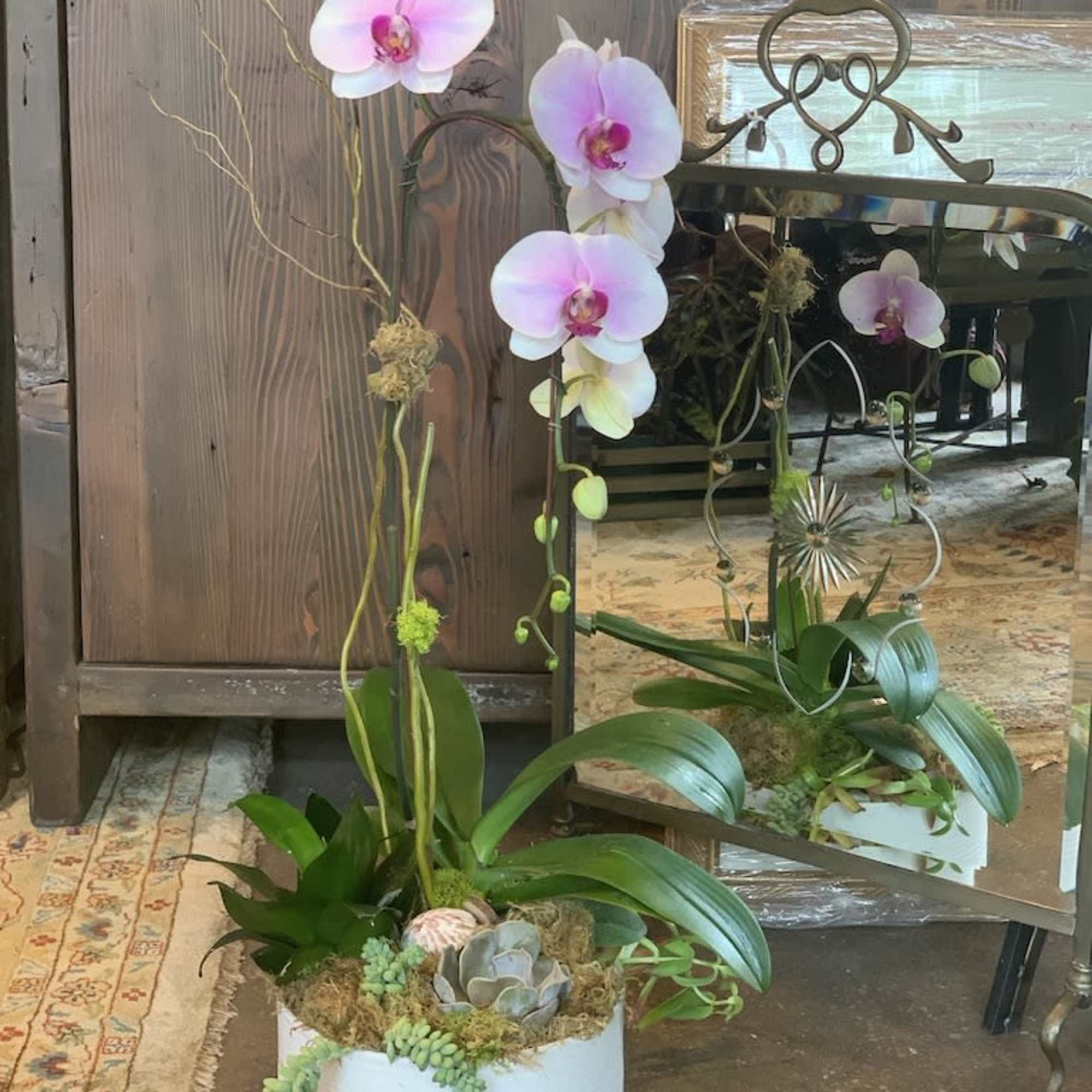 Features a large orchid in full bloom in an arrangement with other