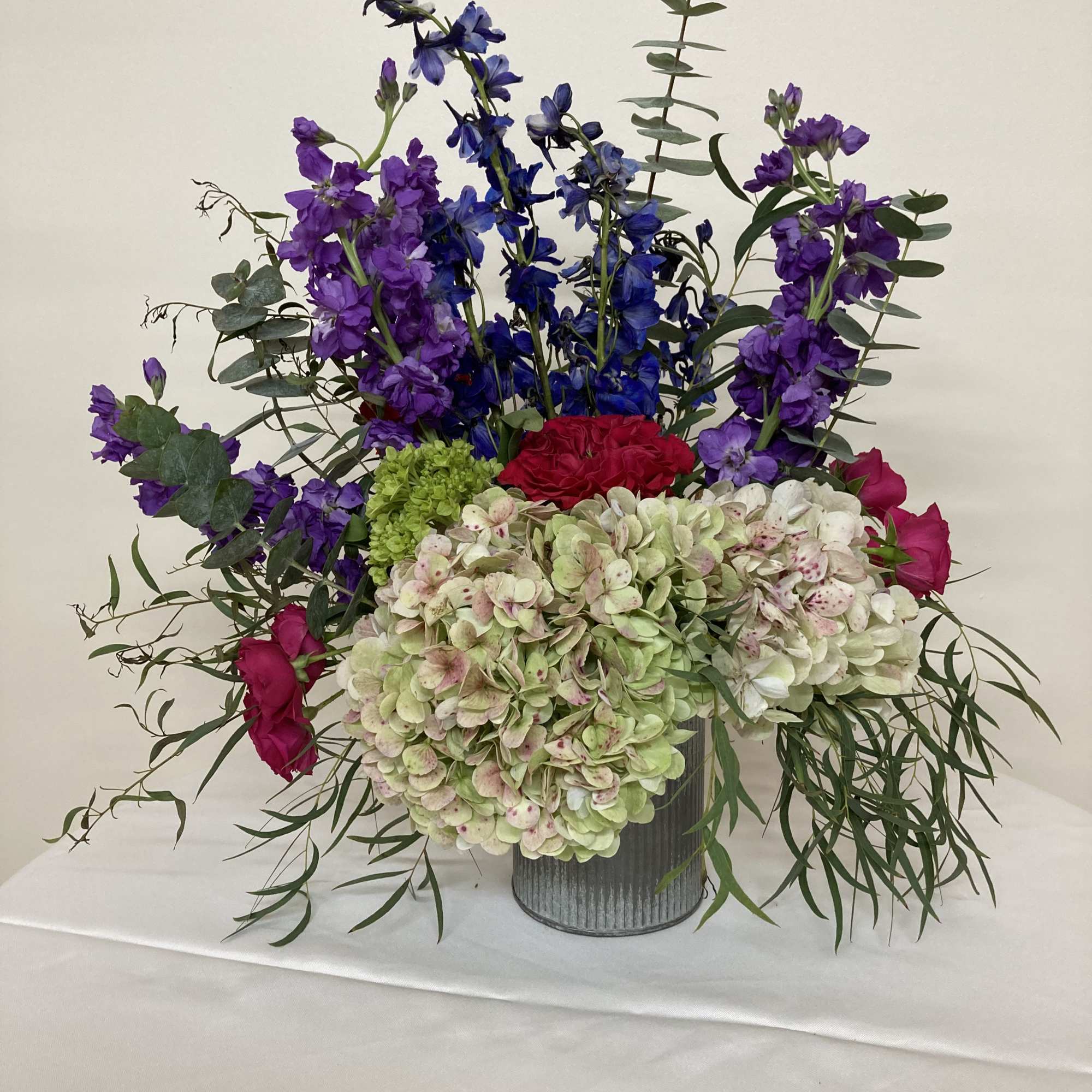 Pink hydrangea, red garden roses, delphinium, purple stock