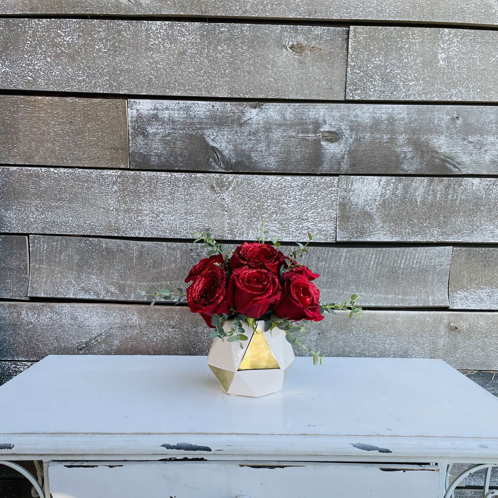 A half dozen red roses glittered in a fashionable bud vase with A half dozen red roses glittered in a fashionable bud vase with