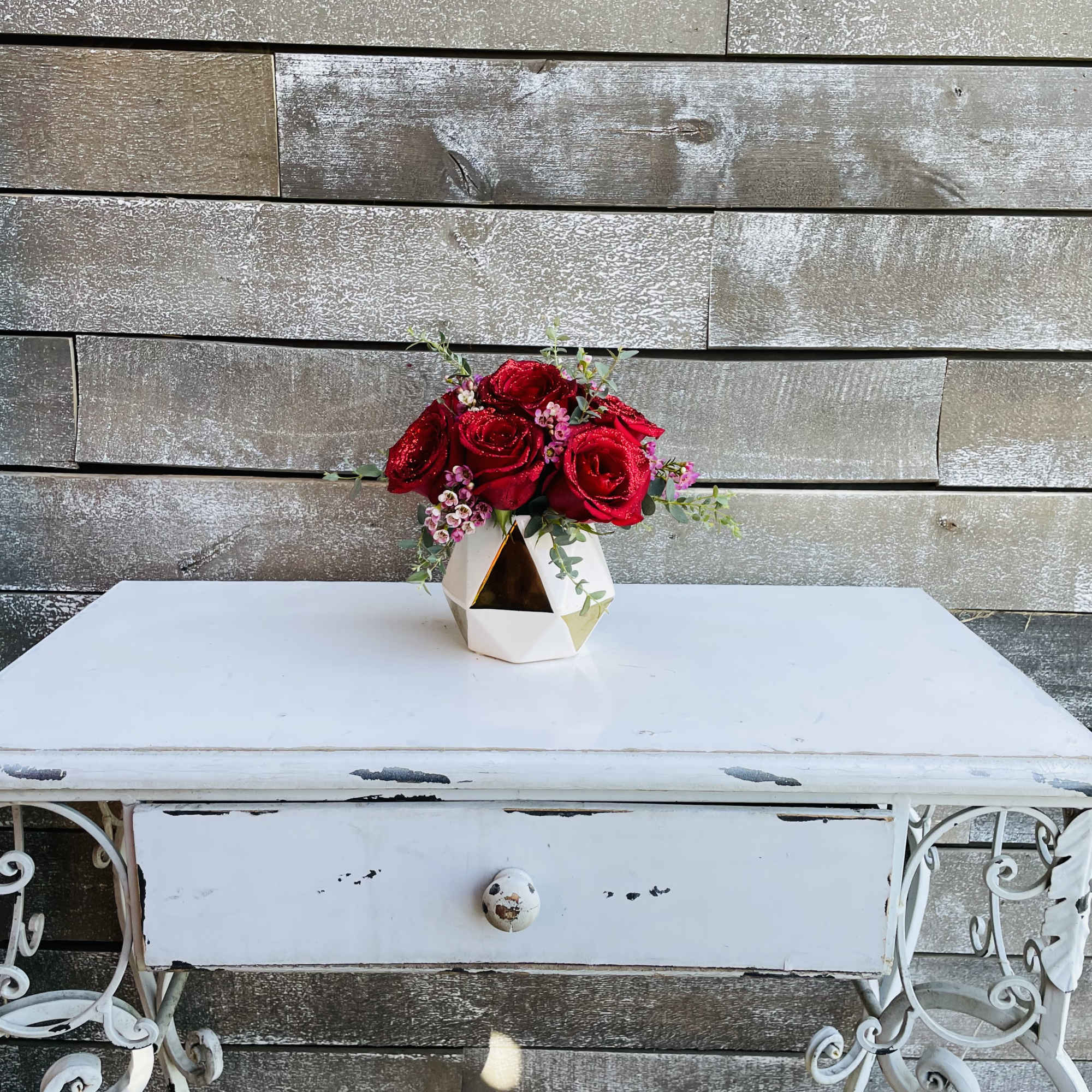 Glittered red roses with greenery and pink waxflower in a white and Glittered red roses with greenery and pink waxflower in a white and