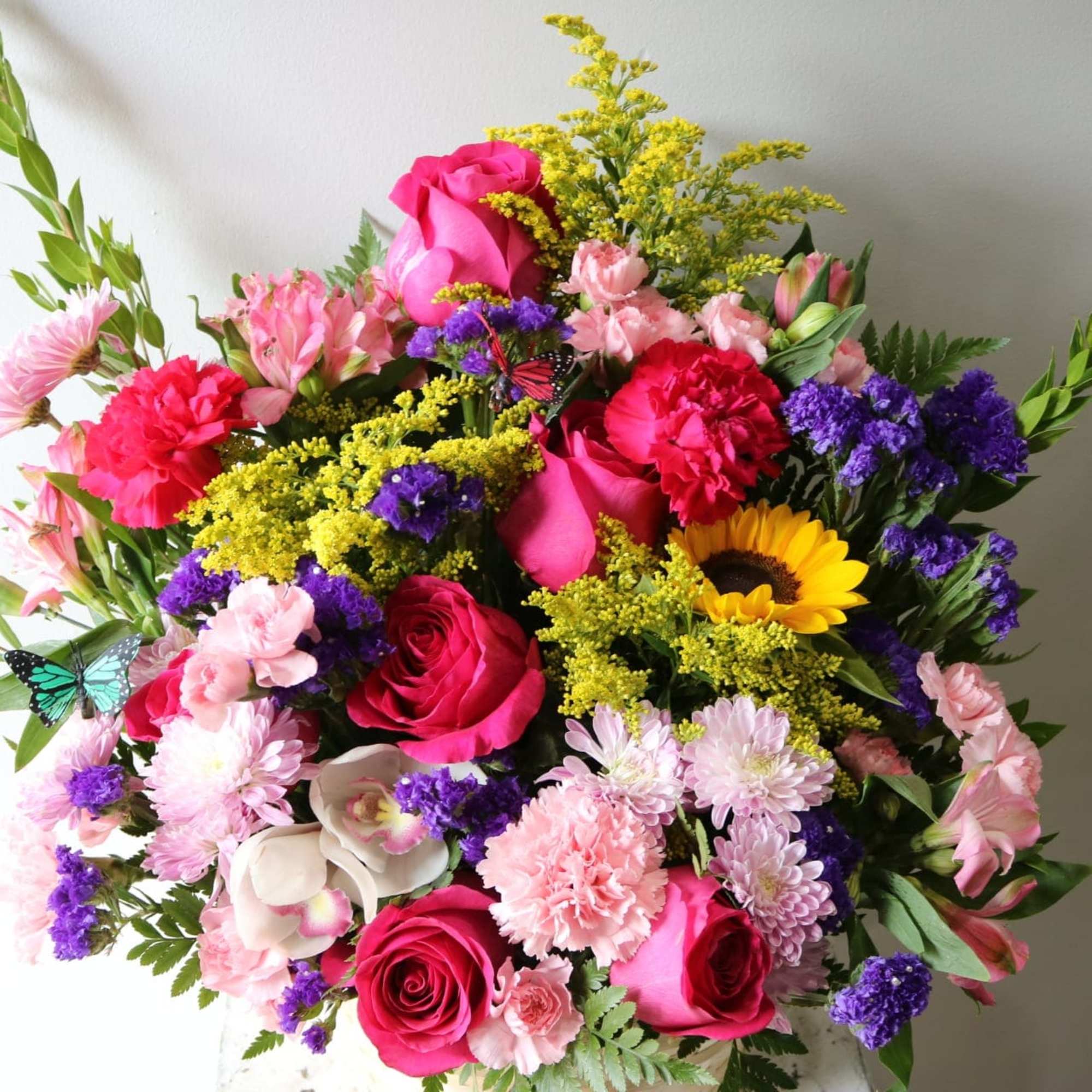 A bright, beautiul basket arrangment with hot pink roses, sunflowers, carnations, cymbidium