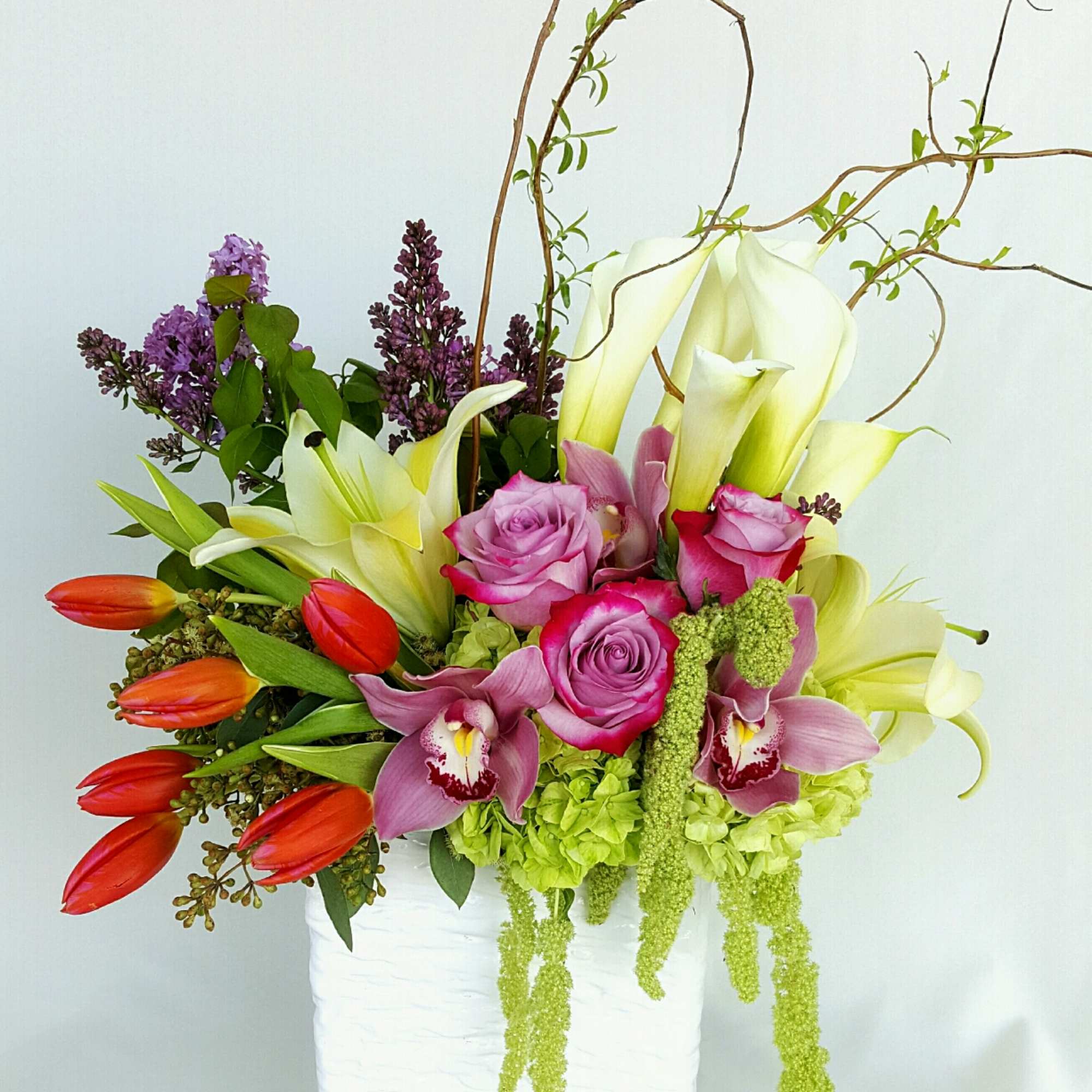 A cheerful arrangement of vibrant orange tulips, lavender roses, a variety of