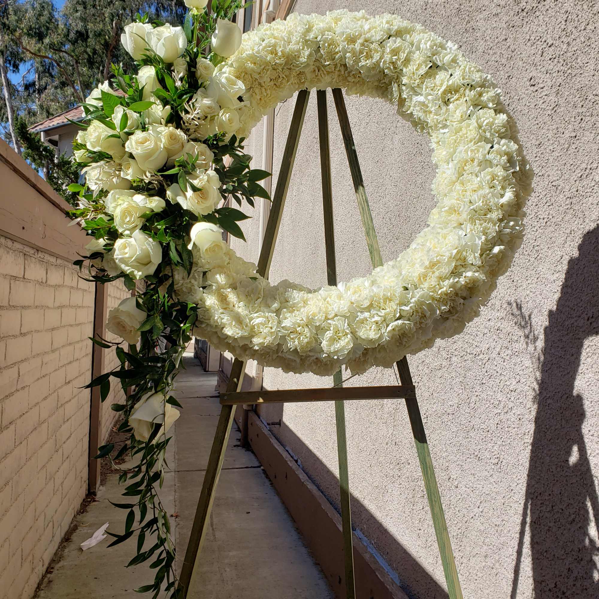 A wreath made with all white carnations. adorned with with white roses