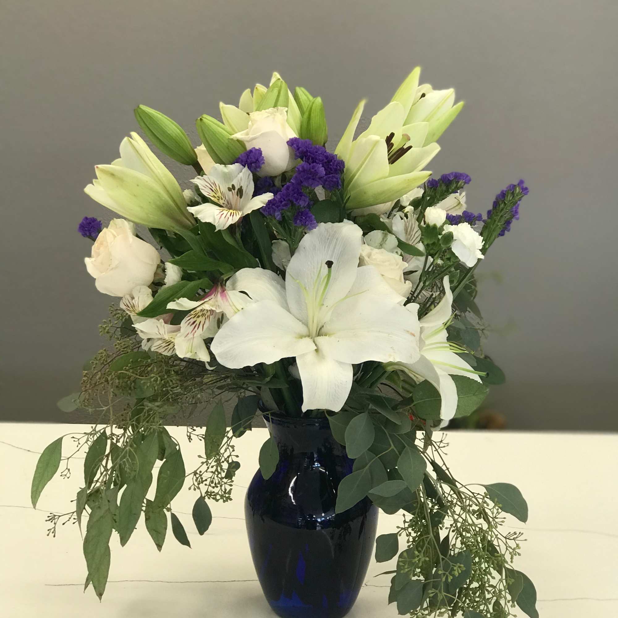 Beautiful white lilies surrounded by cream roses and bursts of purple statice