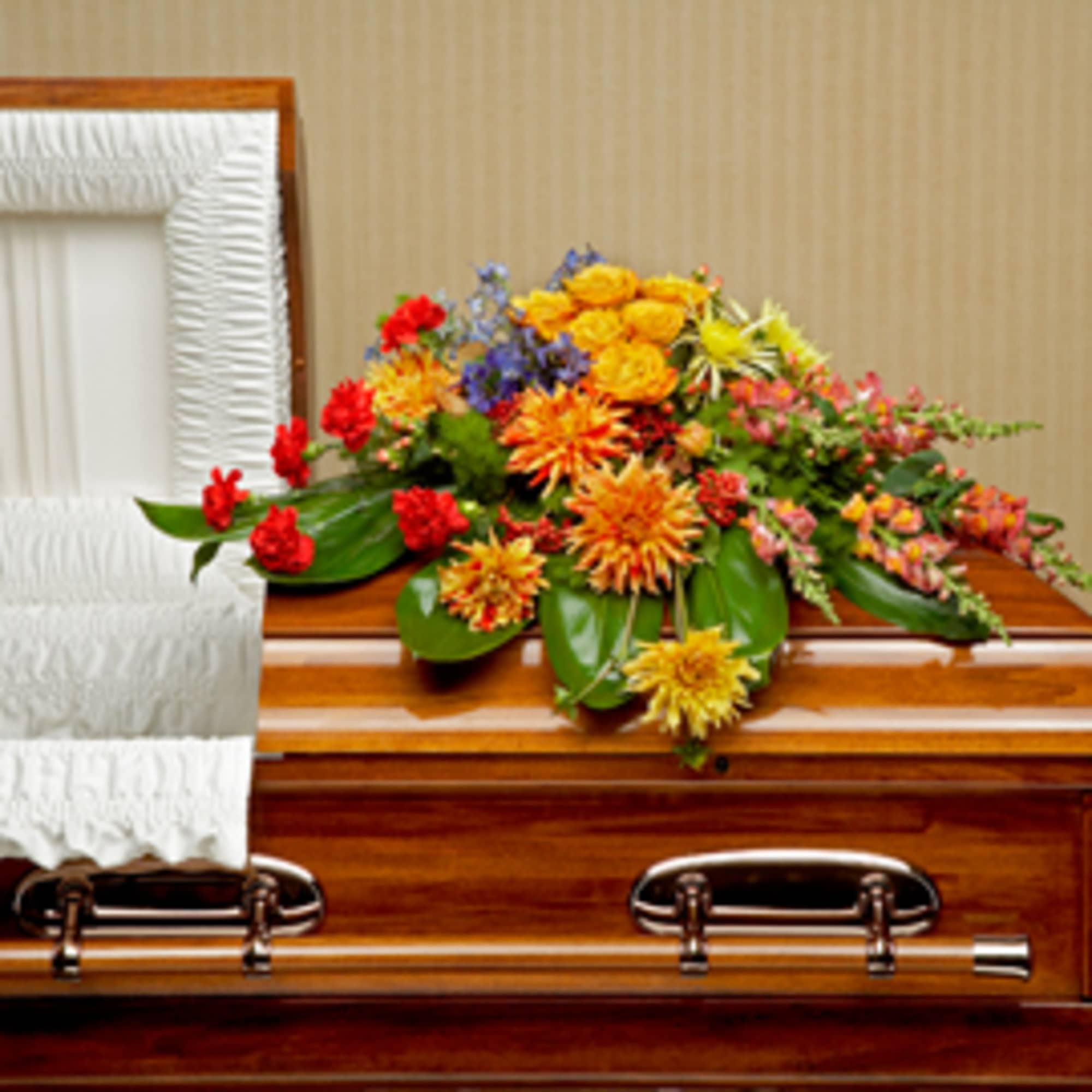 This graceful casket spray of bright blossoms in shades of red, orange This graceful casket spray of bright blossoms in shades of red, orange