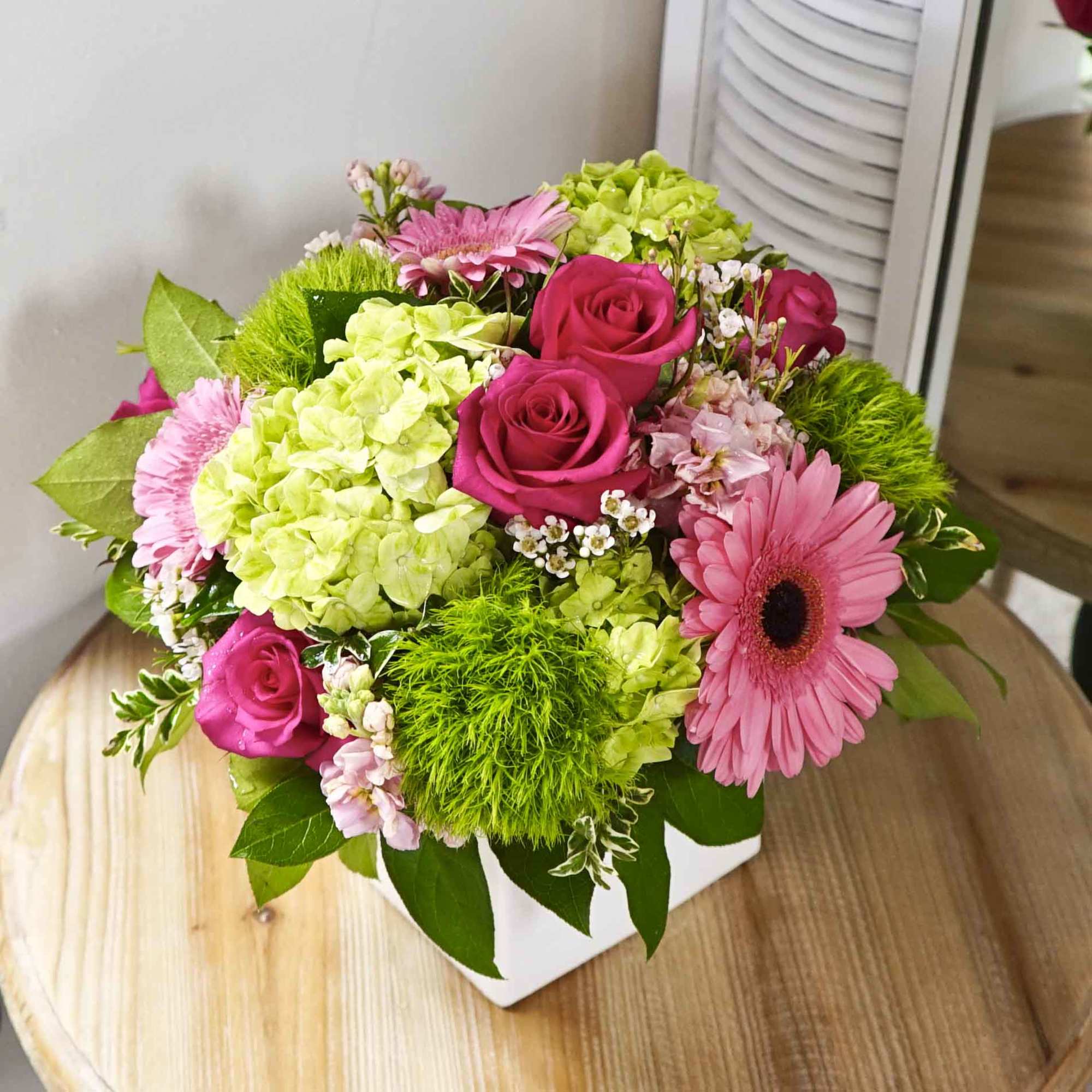 Hot pink roses, pink gerbera daisies, and hydrangeas in white ceramic cube.