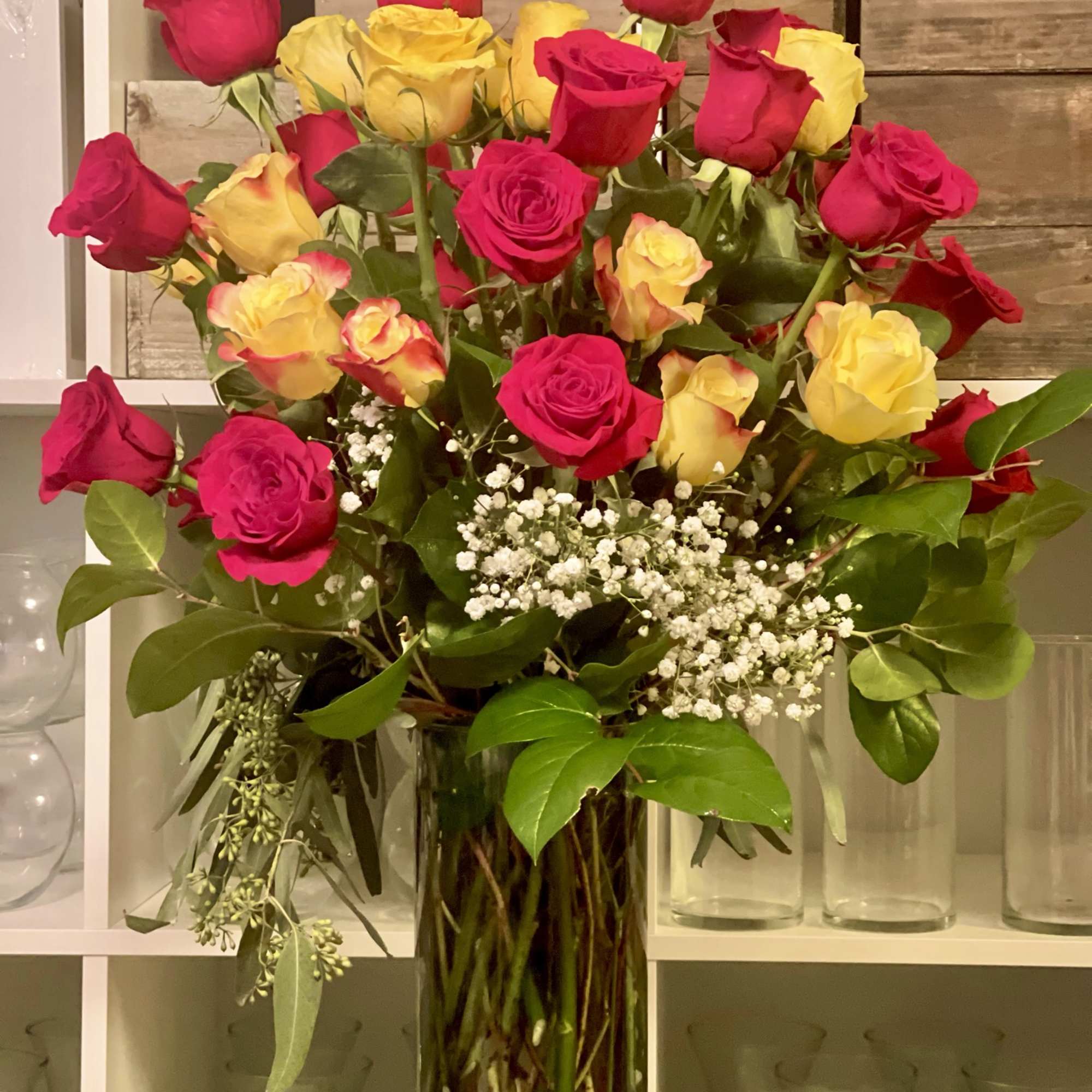 Mixed roses with babies breath and lush greens in a tall cylinder