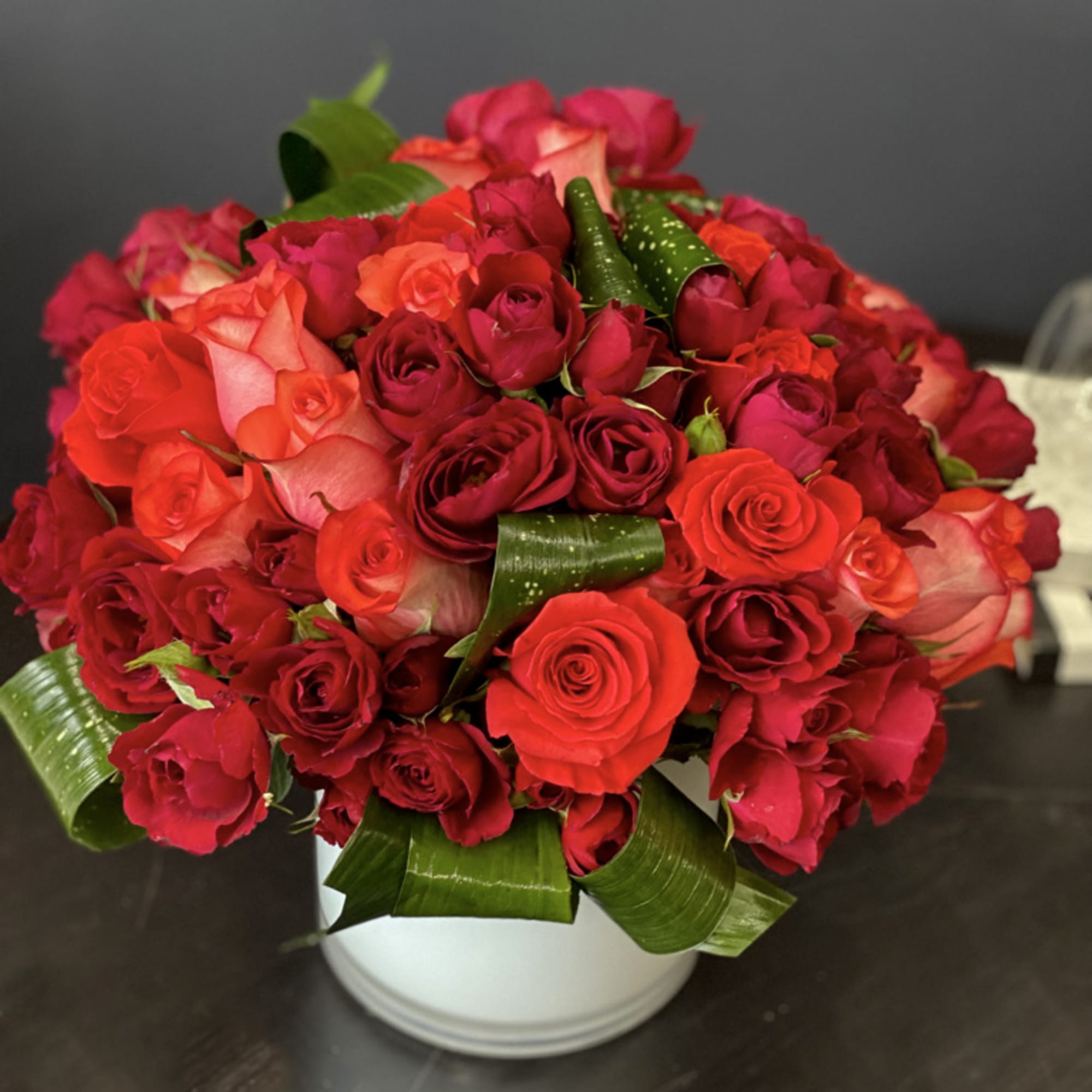 Beautiful arrangement with coral roses, red spray roses and greenery in vase