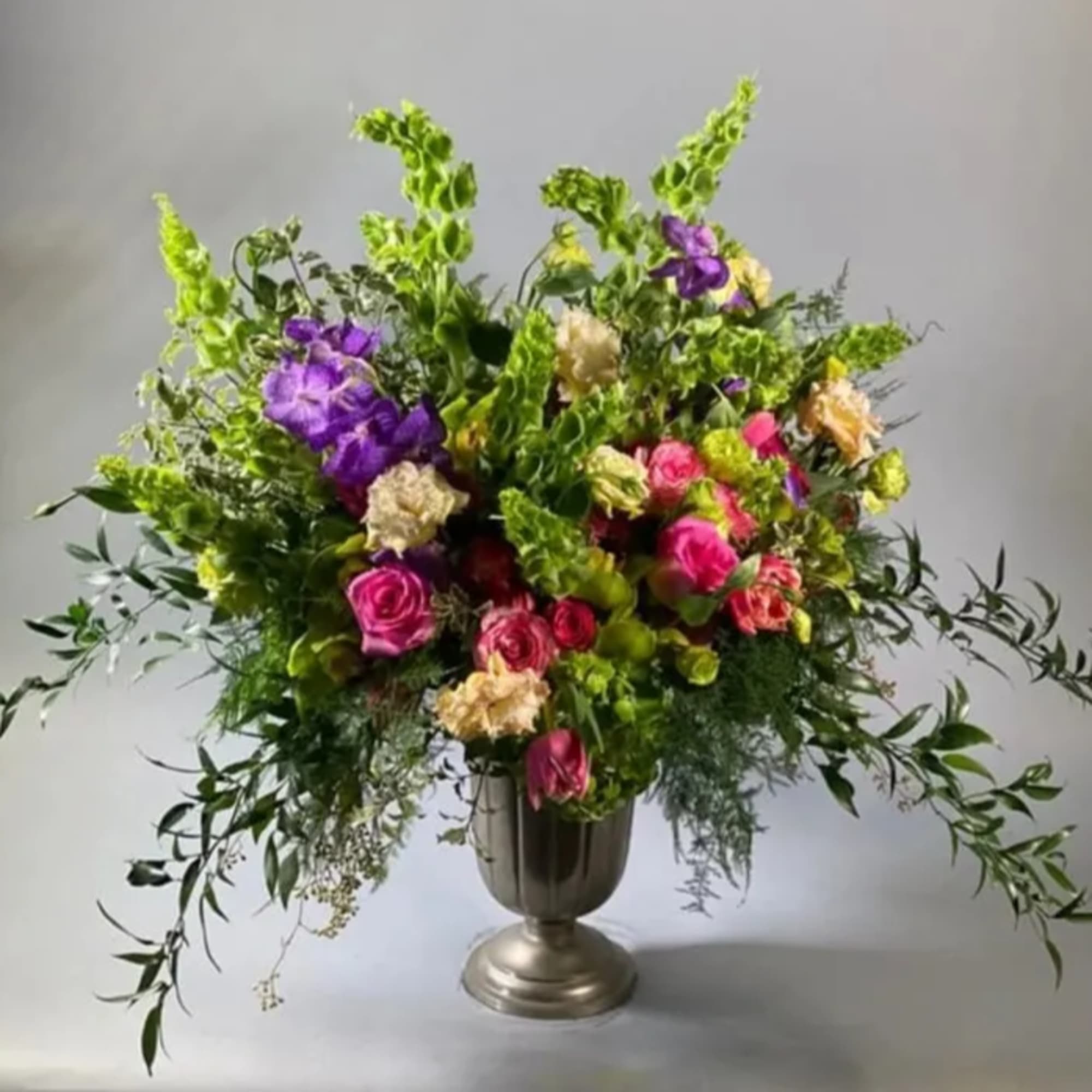This gorgeous array of colorful and luxurious blooms in a metal pedestal