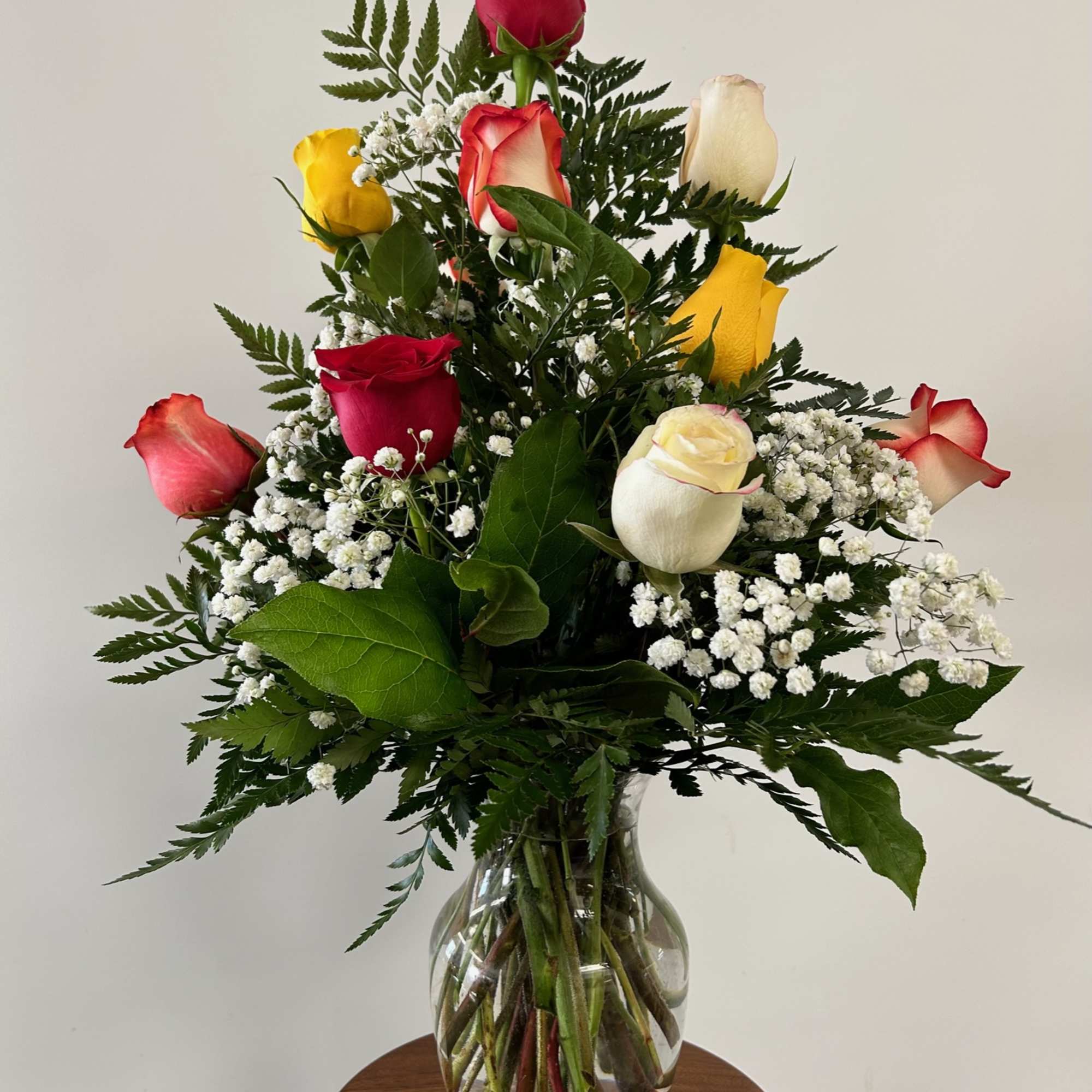 Mixed roses are arranged in a vase with a variety of greenery.
