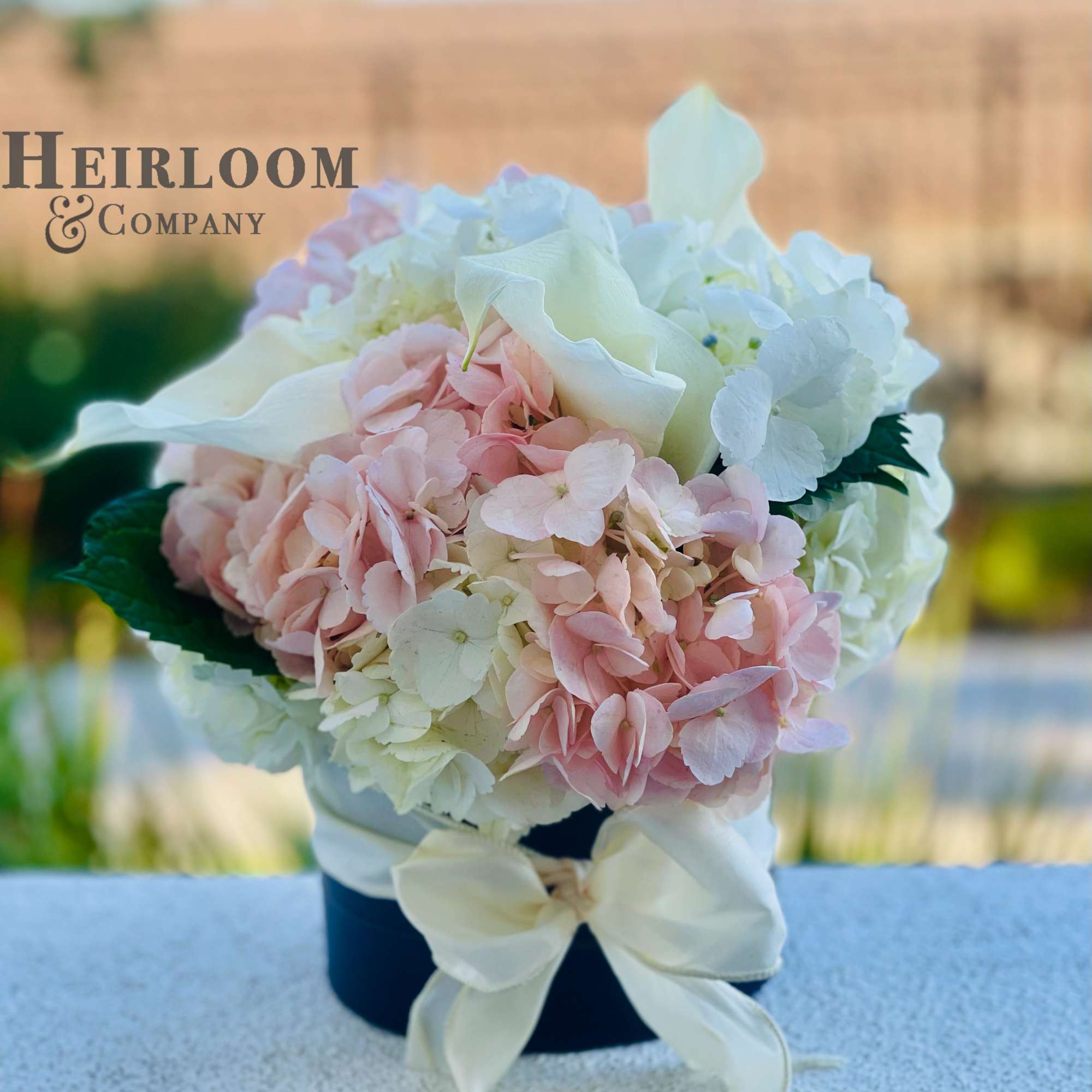 An adorable hatbox filled with blush and white premium hydrangeas and Cala
