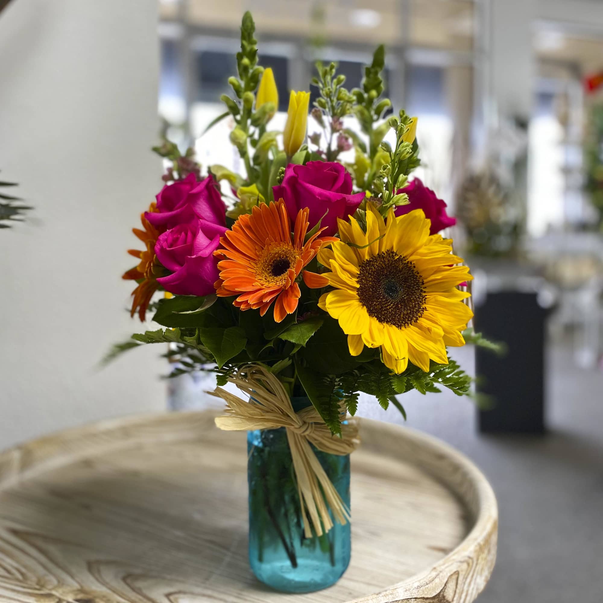 A bright and colorful mix of seasonal flowers design in a mason