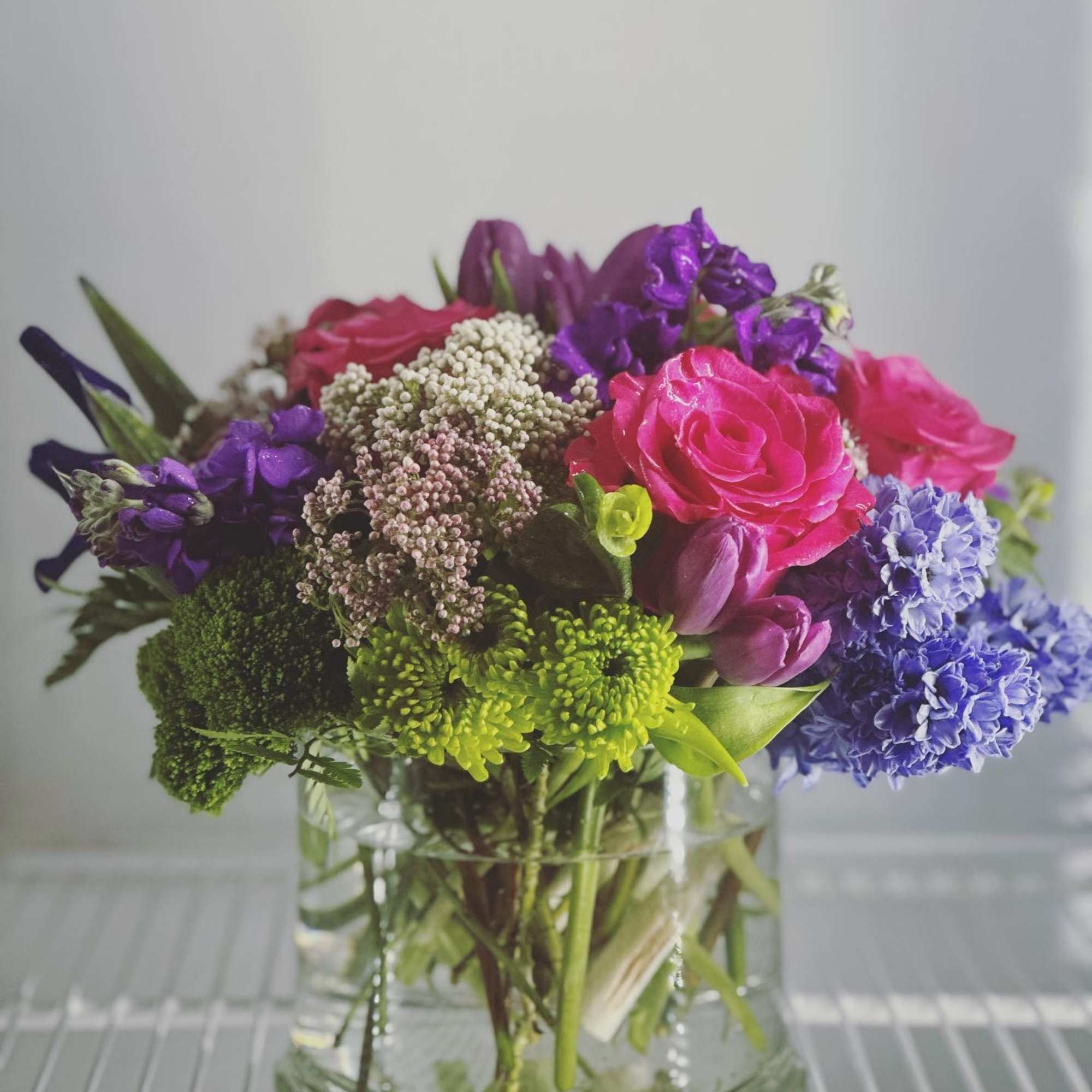 This arrangement includes green dianthus, blue iris, white tulips, hyacinths, and other