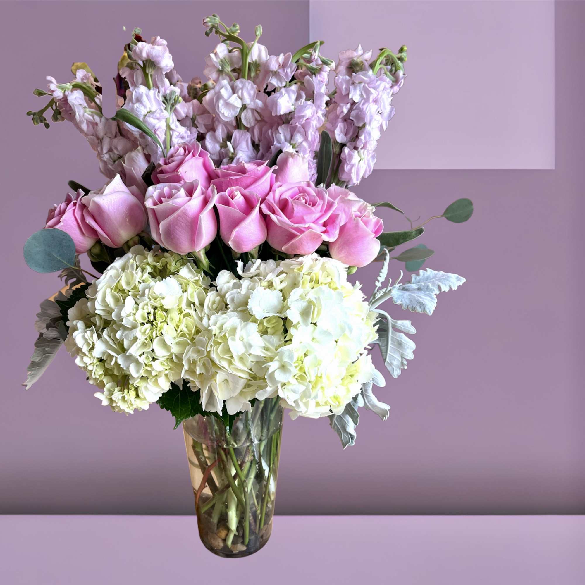 A tall arrangement of hydrangea, roses, and stock with foliage in a