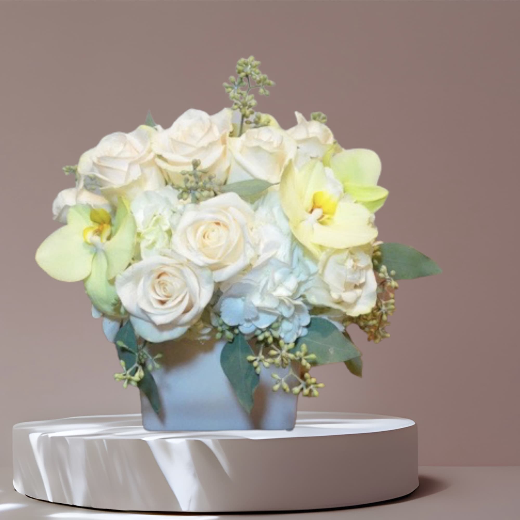 Soft roses, hydrangea, orchids, and eucalyptus in a ceramic vase make a