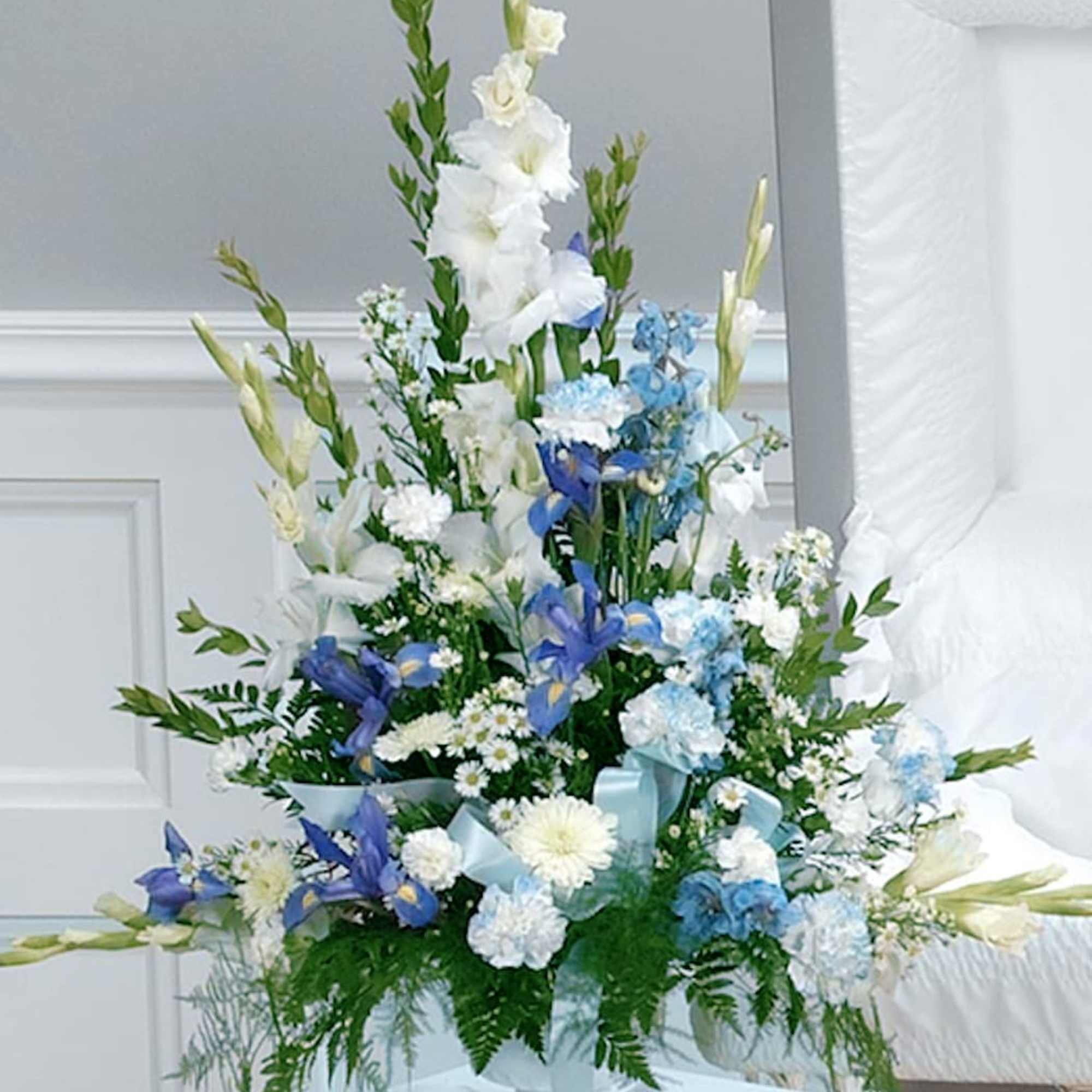 Pedestal arrangement including delphinium, iris and carnations with white gladiolas and cushion