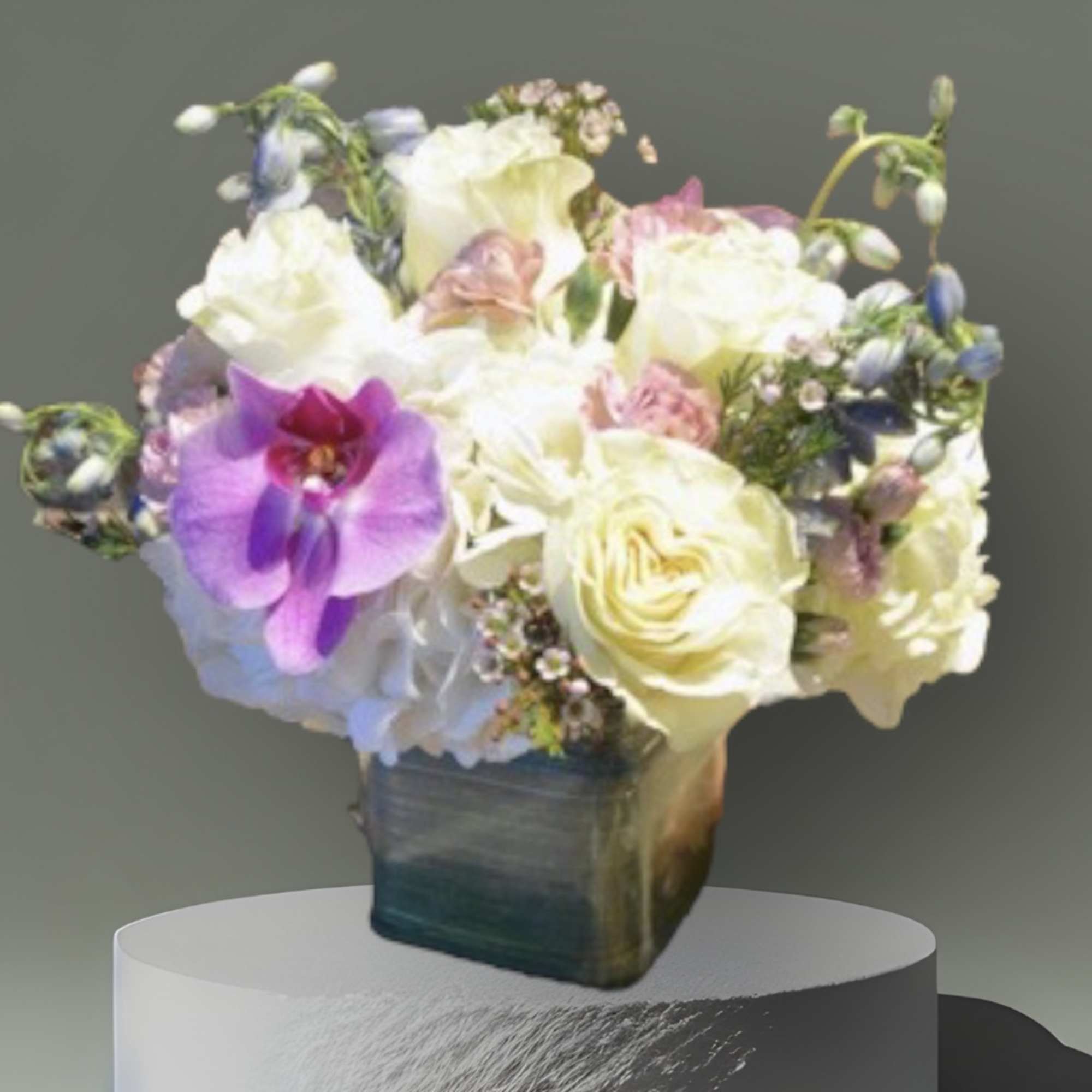 A soft, sweet arrangement of hydrangea, cream roses, orchids, blue delphinium, and