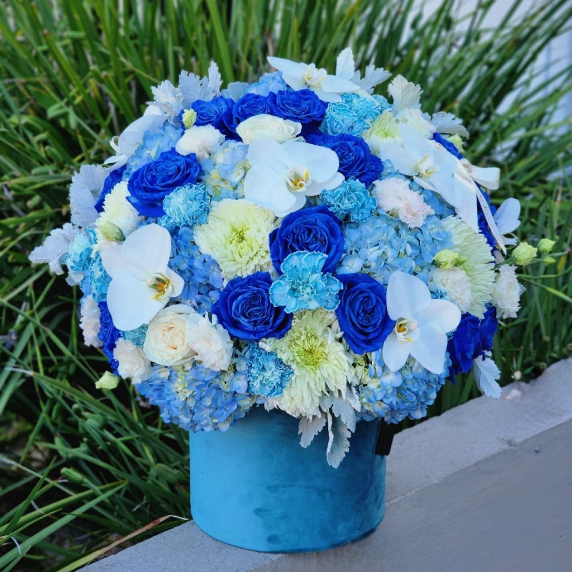 This blue-themed floral arrangement with blue hydrangeas, roses, and carnations, complemented by
