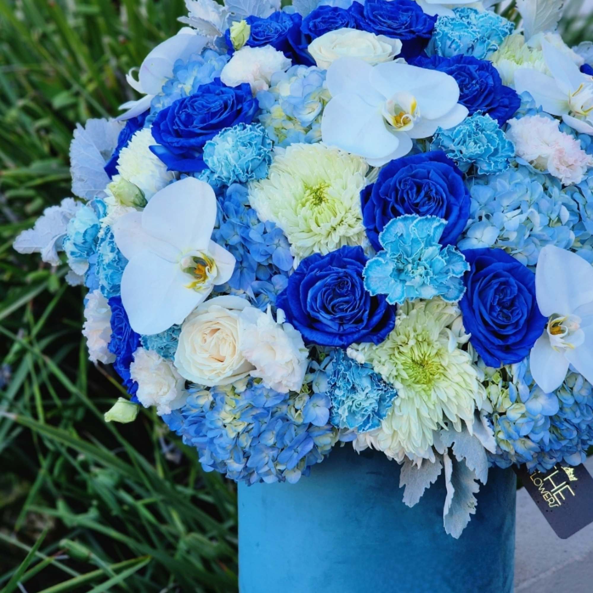 This blue-themed floral arrangement with blue hydrangeas, roses, and carnations, complemented by