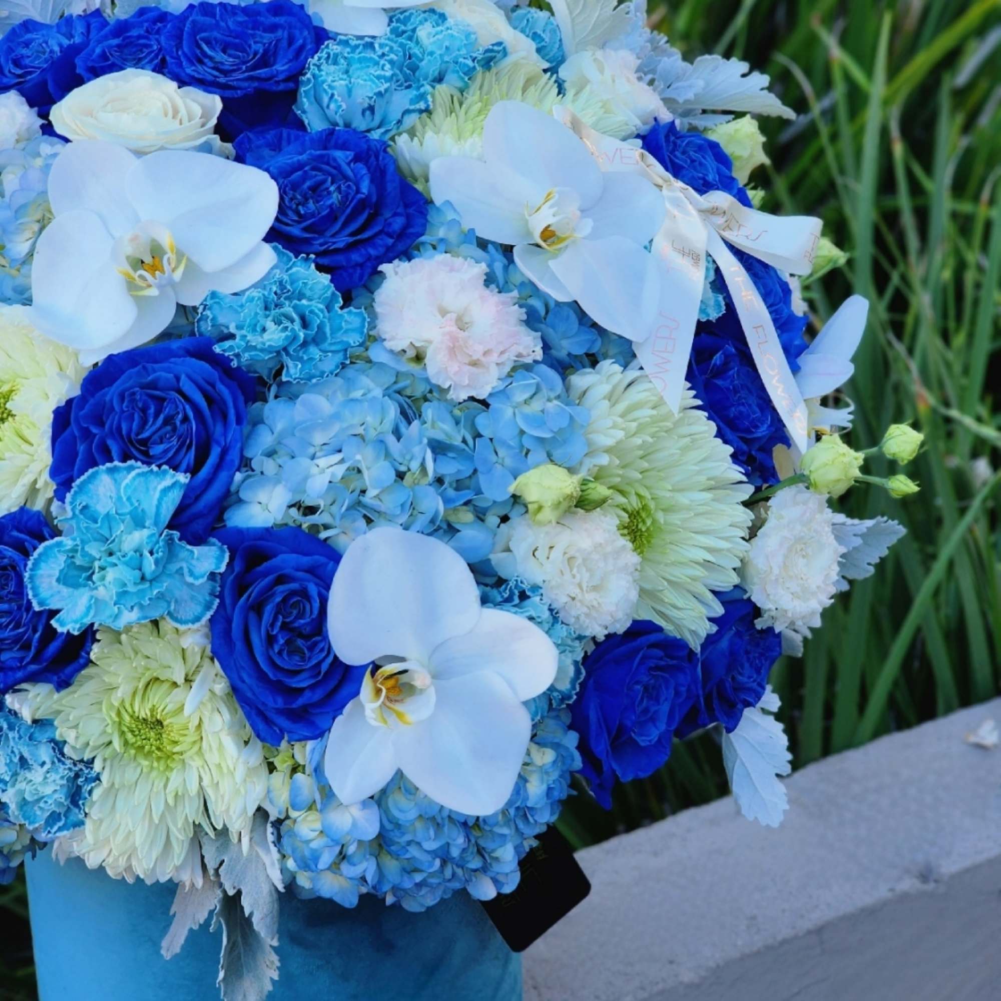 This blue-themed floral arrangement with blue hydrangeas, roses, and carnations, complemented by