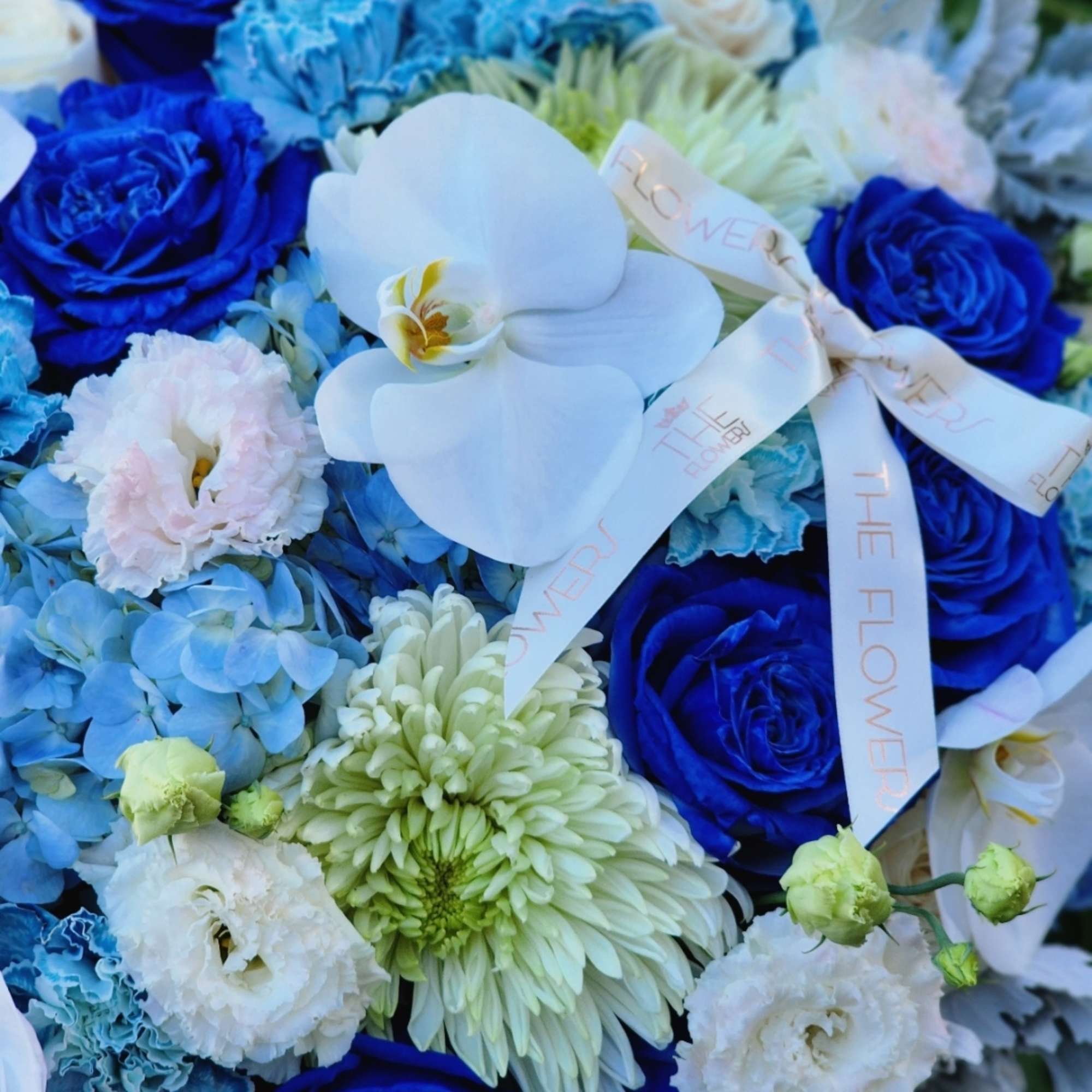 This blue-themed floral arrangement with blue hydrangeas, roses, and carnations, complemented by