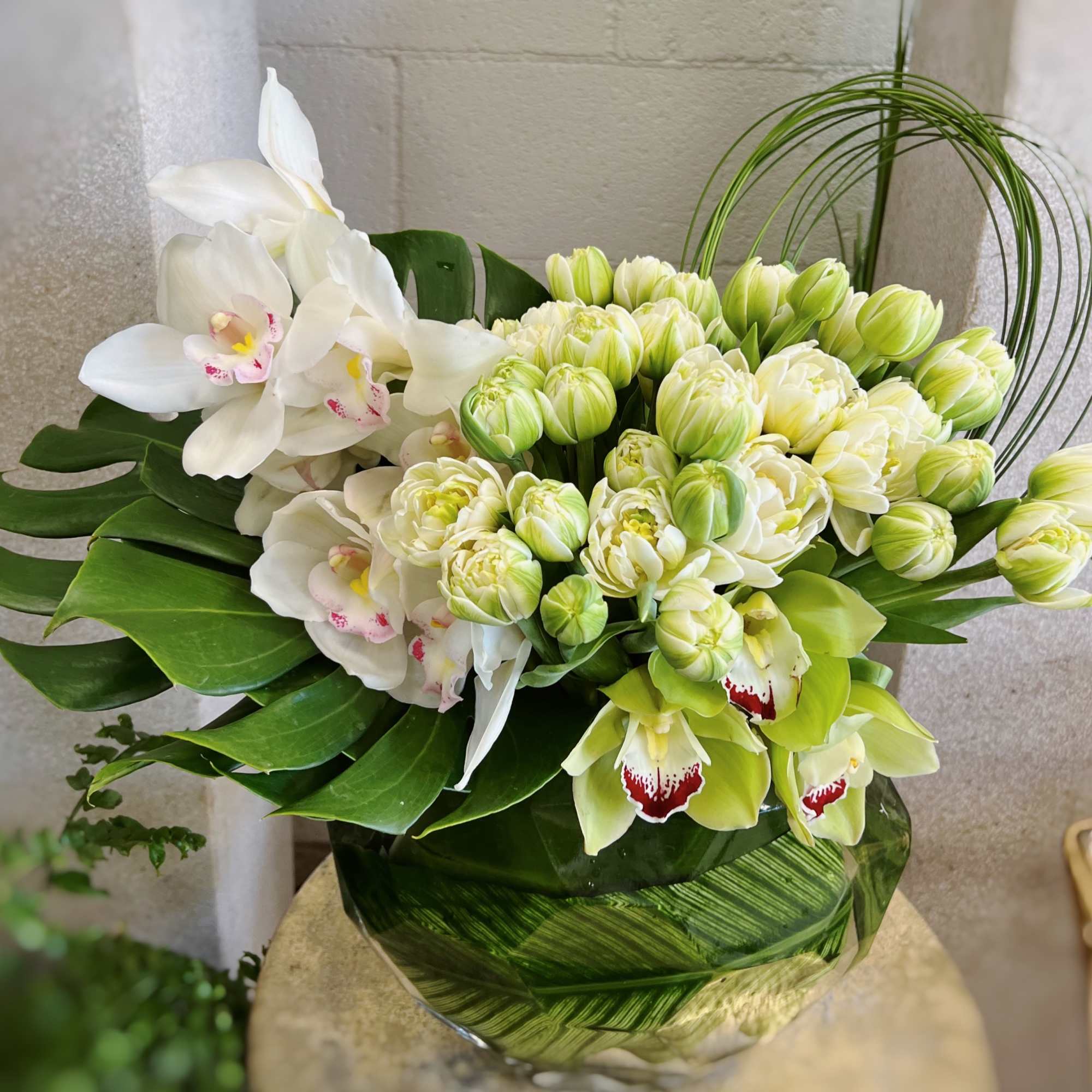 In a leafed line vase, this arrangement has white orchids, along with