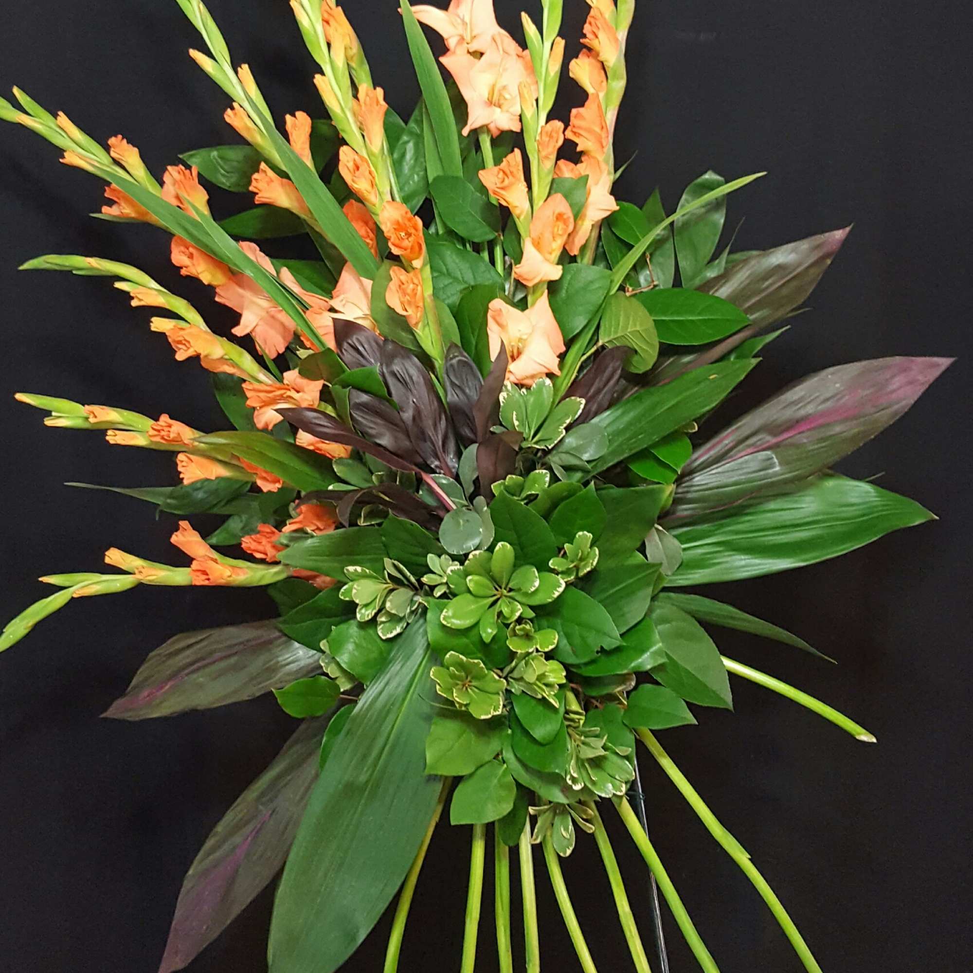 This standing spray features a fan of gladiolus and aspidistra mixed with This standing spray features a fan of gladiolus and aspidistra mixed with