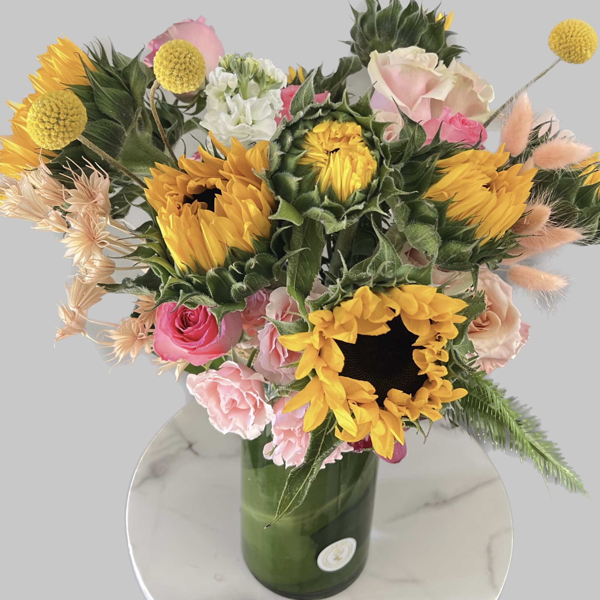 This arrangement includes  sunflowers ,roses and seasonal blooms It is the