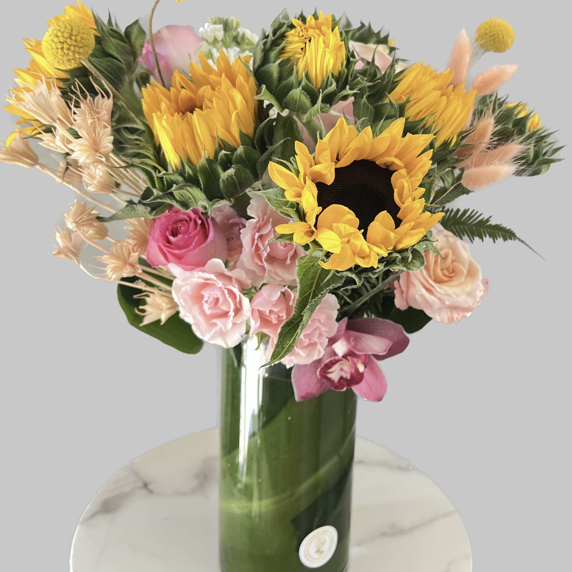 This arrangement includes  sunflowers ,roses and seasonal blooms It is the