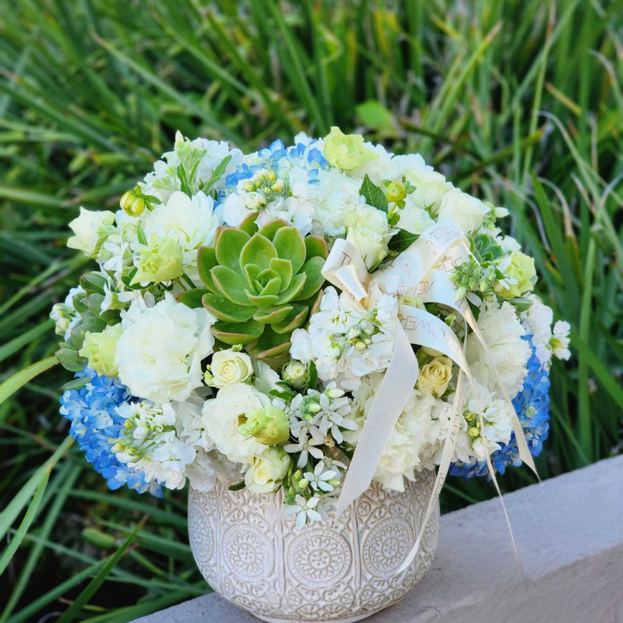A succulents, blue hydrangeas, and white flowers floral arrangement in a vase