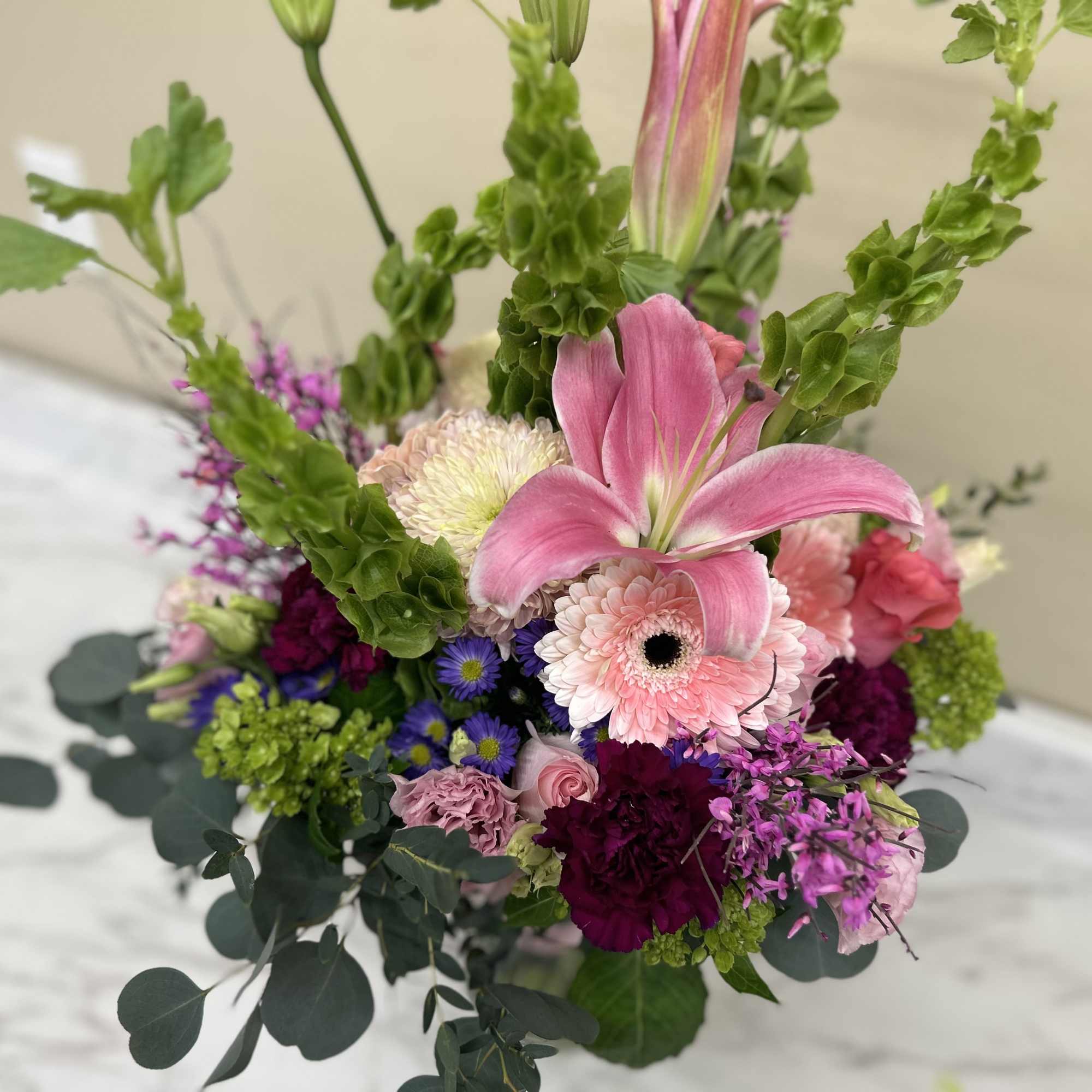 Pinks purple green and a mix of greenery in vase