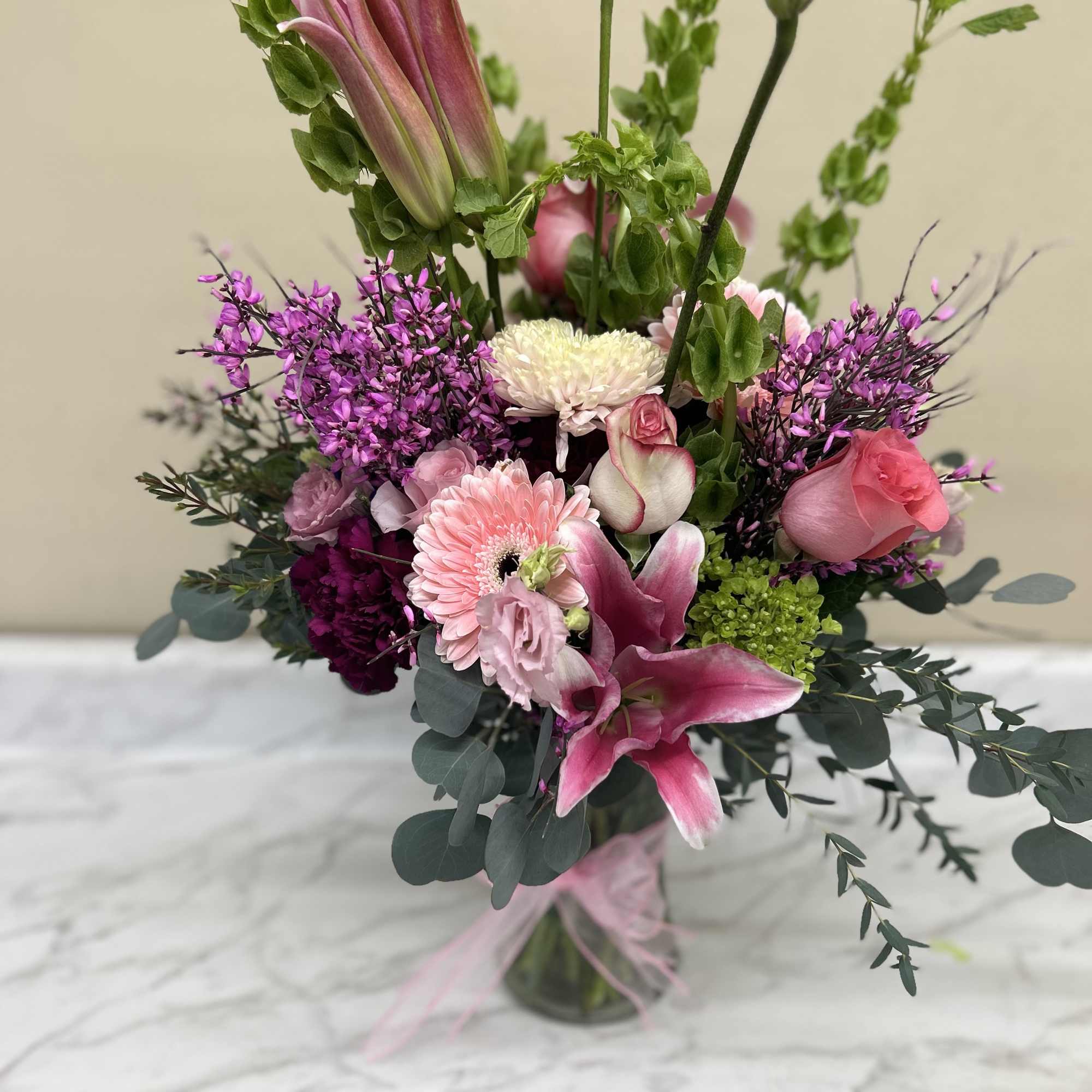 Pinks purple green and a mix of greenery in vase