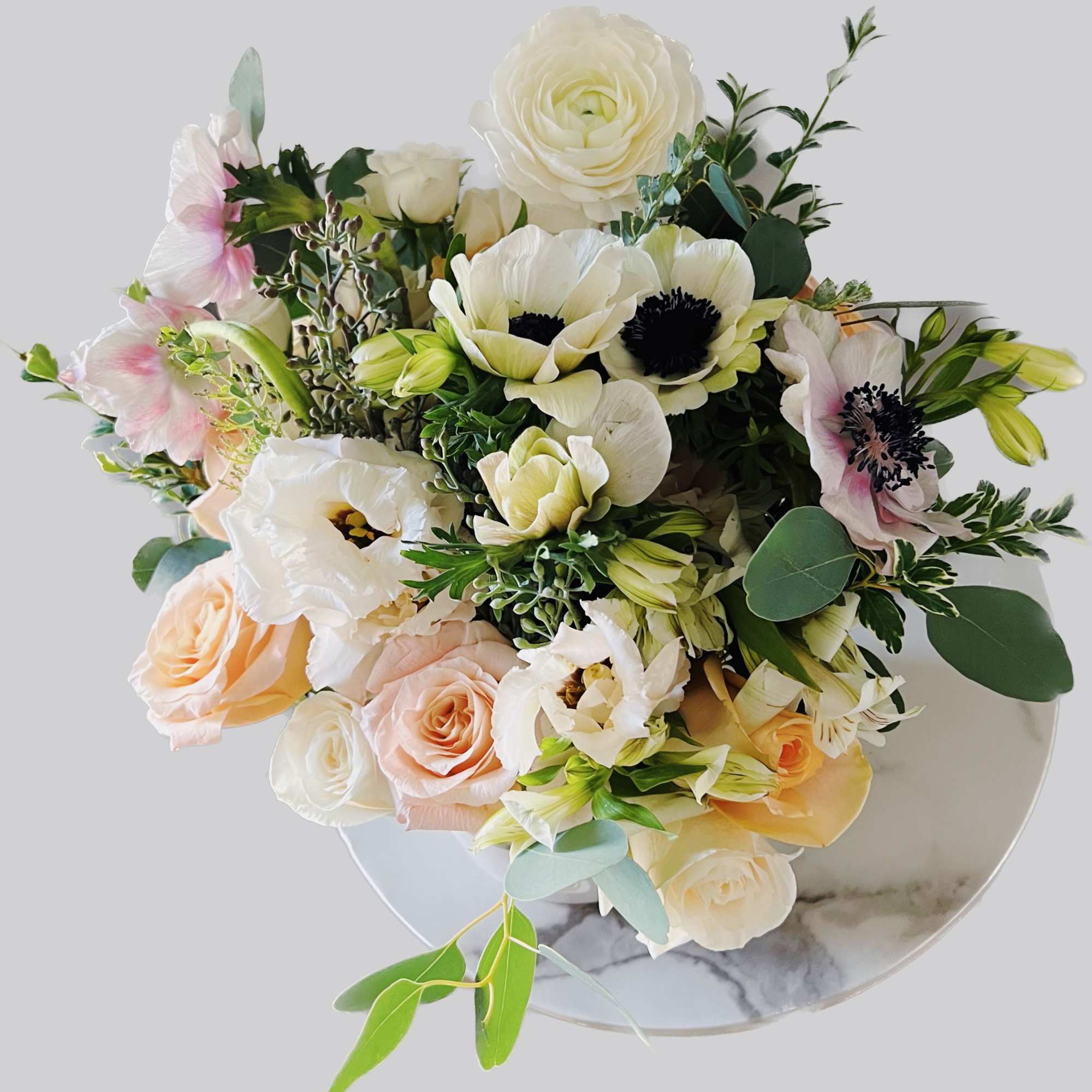 This garden lush style arrangement includes roses, anemones and seasonal blooms. This
