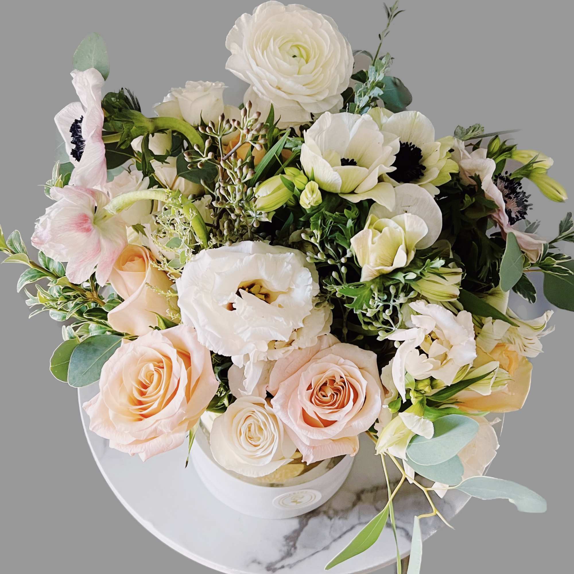 This garden lush style arrangement includes roses, anemones and seasonal blooms. This